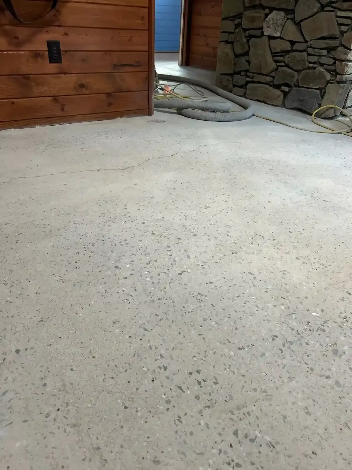 A concrete floor in a room with a wooden wall and a stone fireplace.
