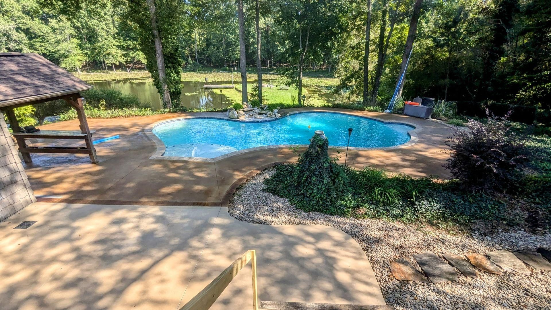 A large swimming pool surrounded by trees and a gazebo in a backyard.