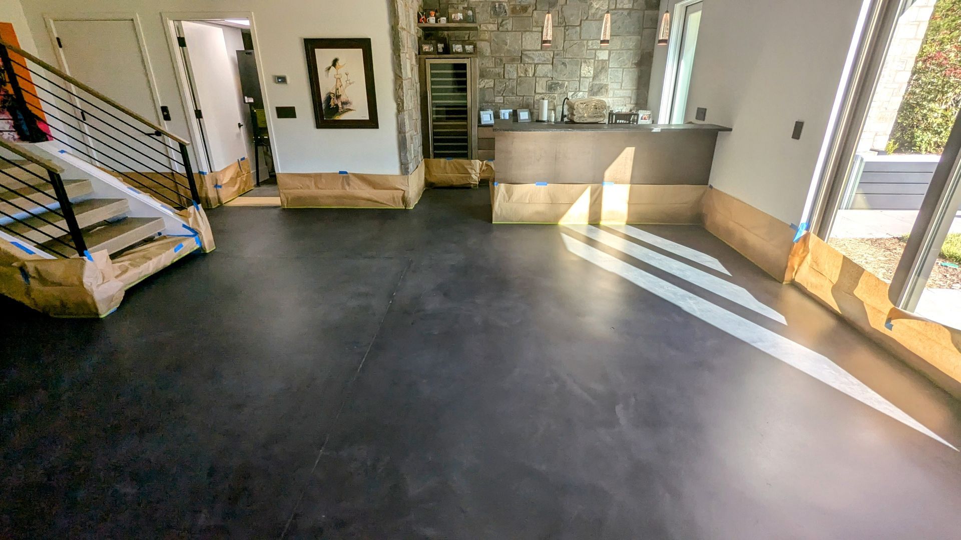 A living room with a black floor , stairs , and a kitchen.