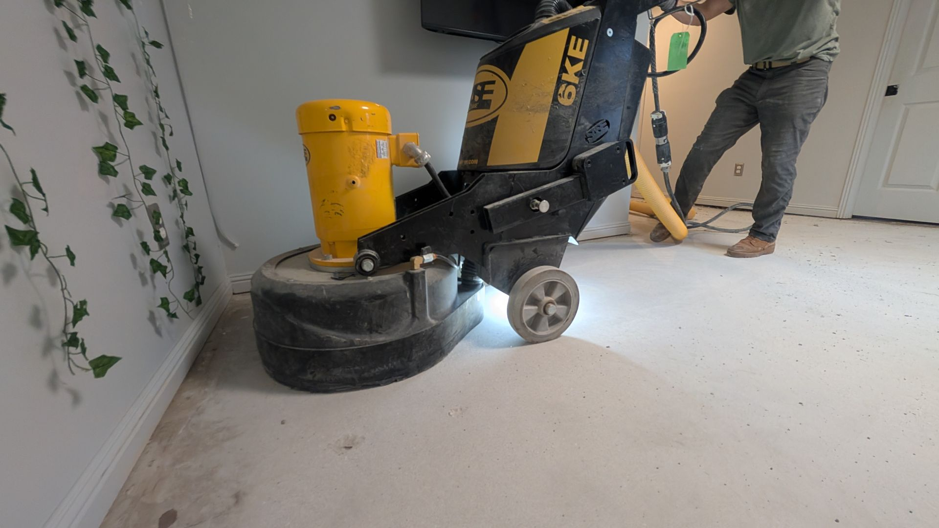 Worker using a concrete floor grinder to smooth an interior surface during surface preparation for coating or polishing.