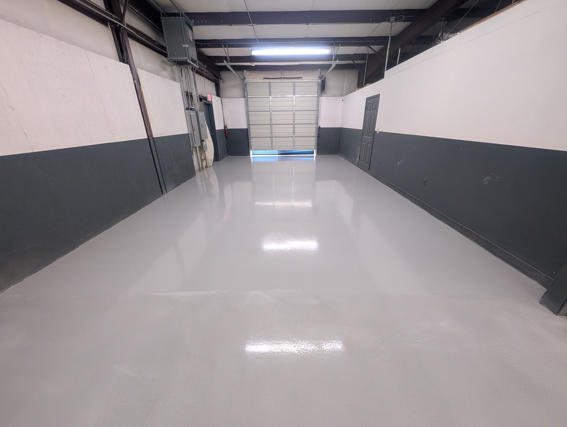 A wide shot of a modern, empty breakroom with glossy concrete floors, white cabinets, kitchen appliances, and metal tables.