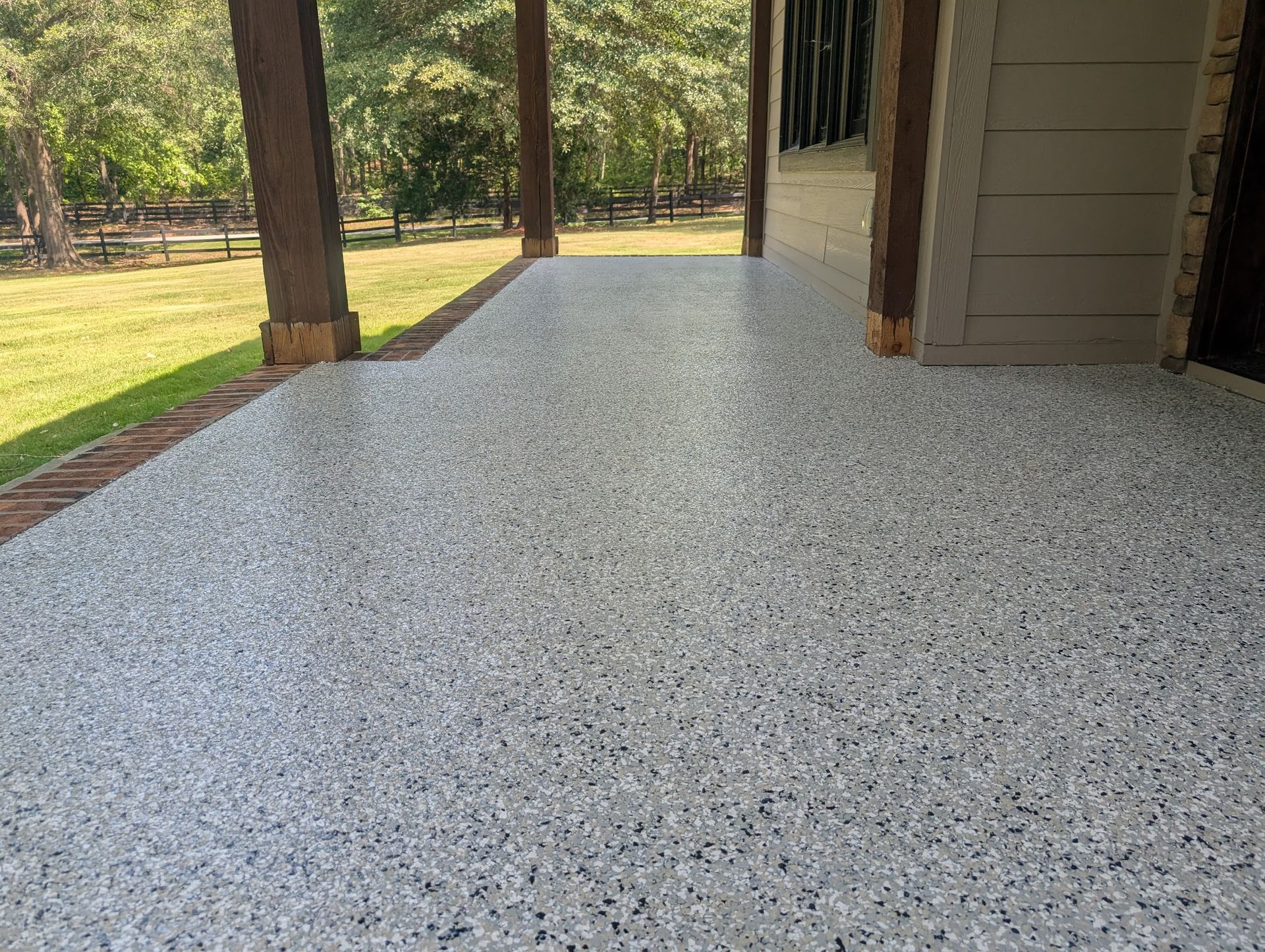 Epoxy-coated patio with speckled finish under covered porch, surrounded by greenery in Greenville, SC.