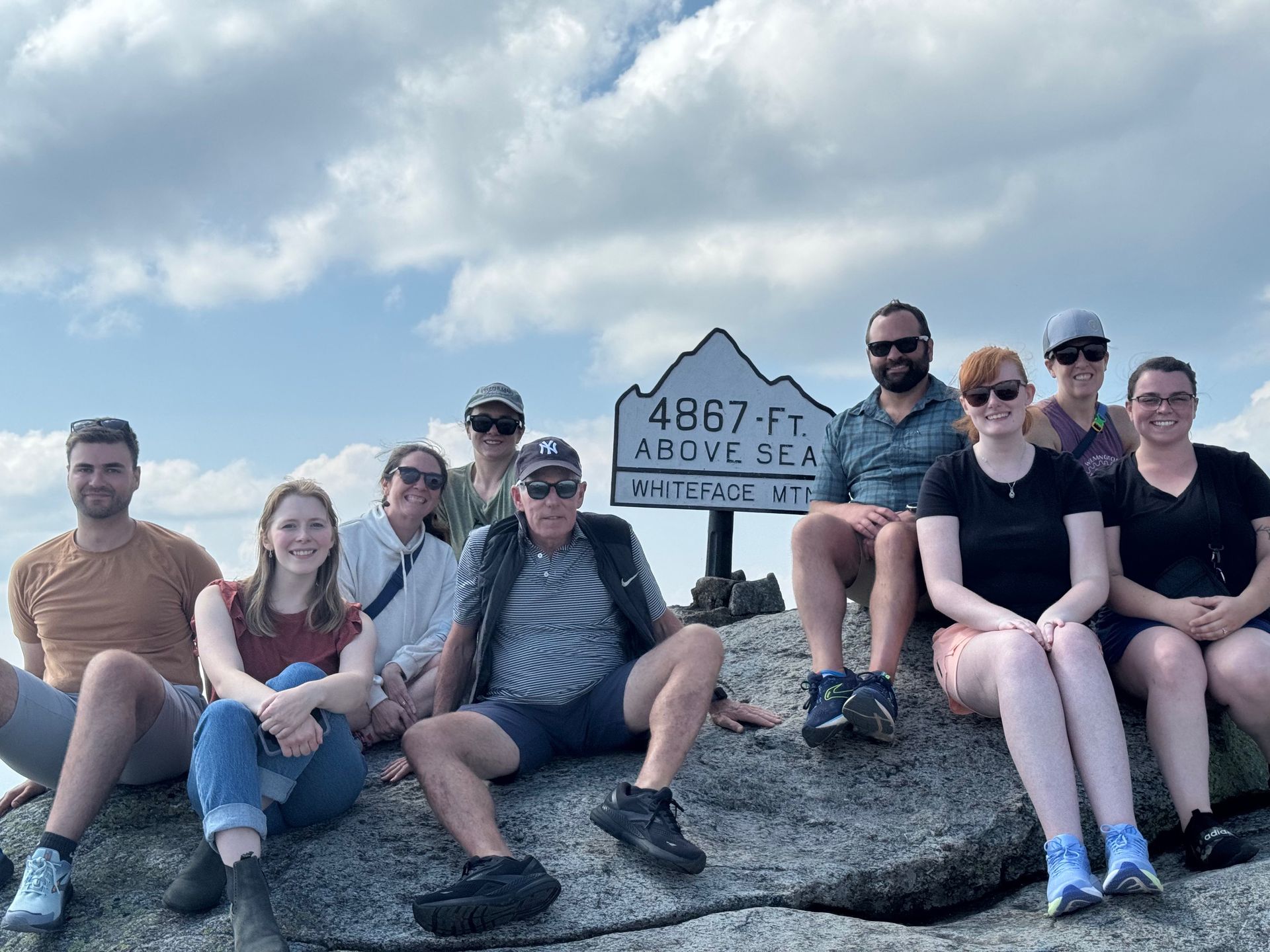 Flink Maswick Law team on a rocky summit, posing near a sign on Whiteface Mountain that reads 