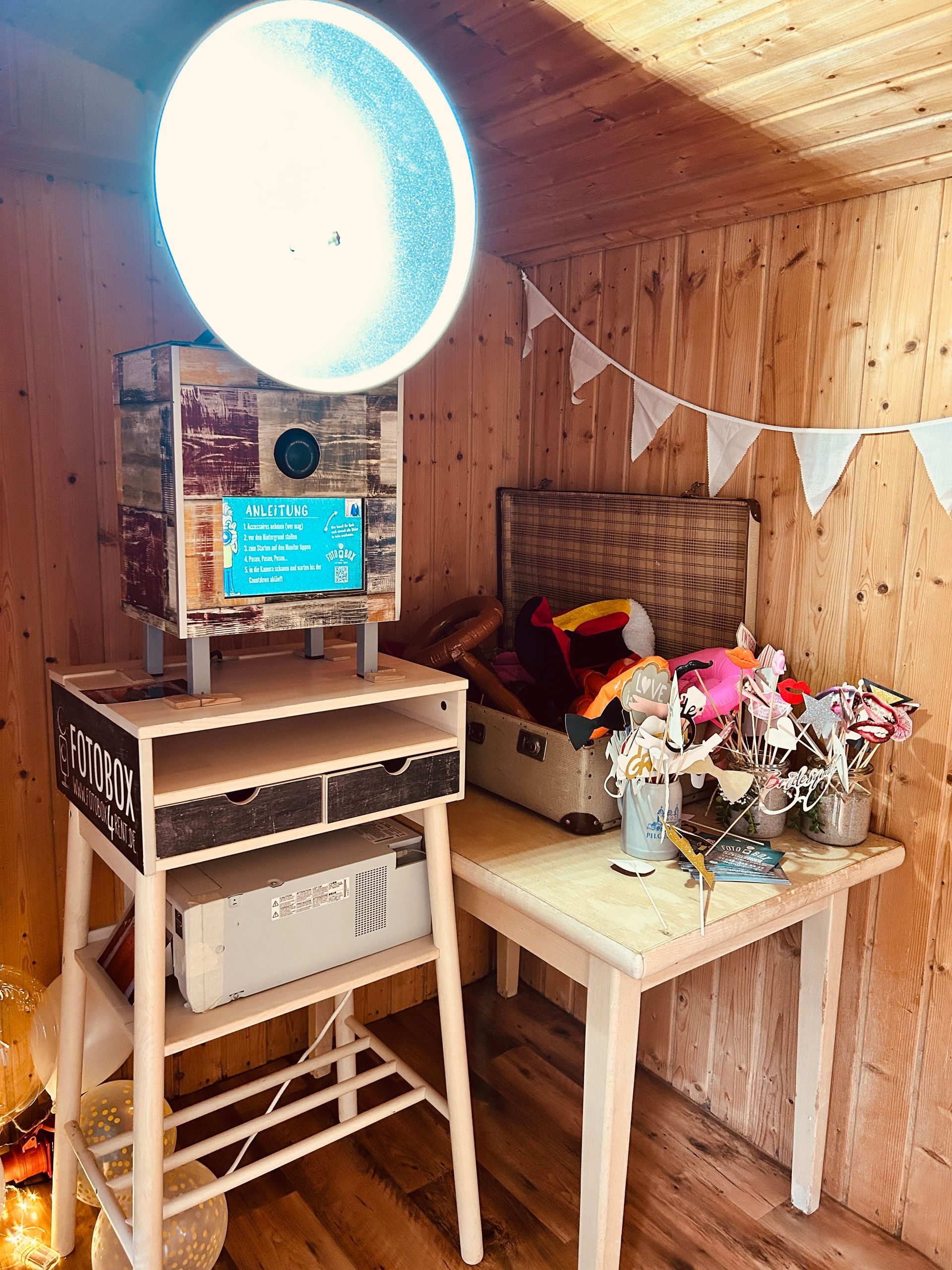 Ein holzgetäfelter Raum mit einer leuchtenden runden Lampe, einem Keyboardständer, einem kleinen Tisch und Blumen auf einer Bank.