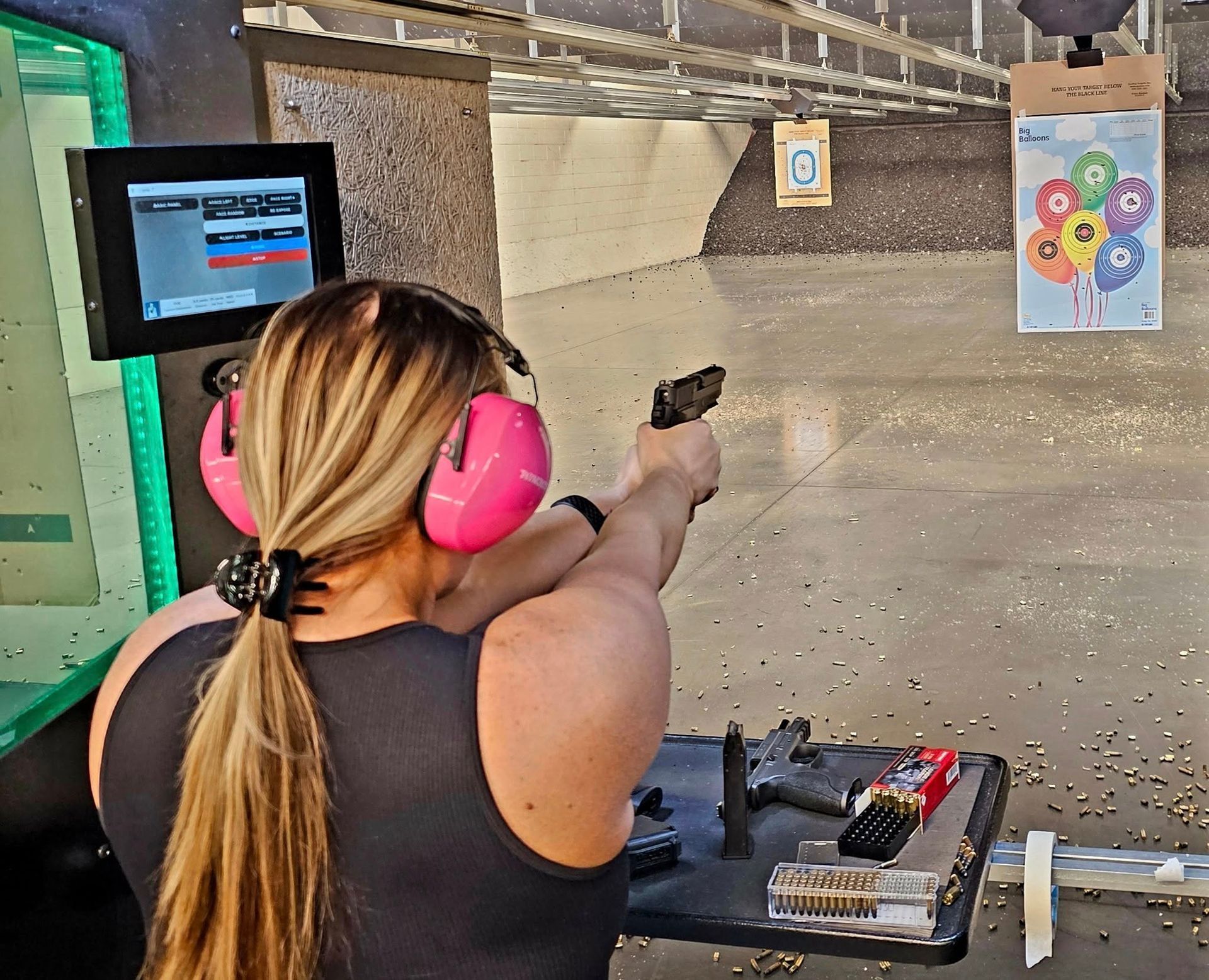 Woman in pink ear protection shooting a pistol at a lane

