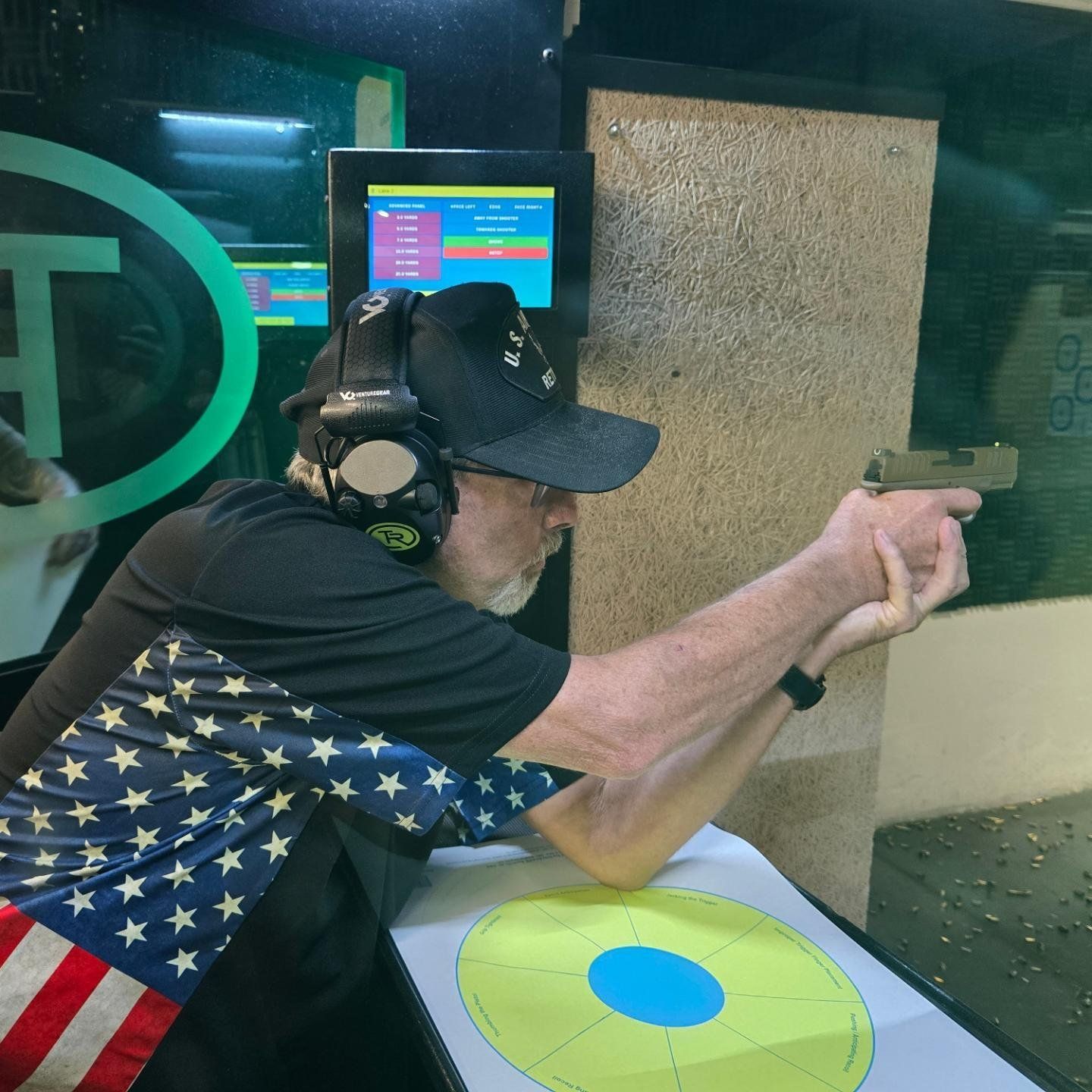 Older man shooting at a target beside an American flag
