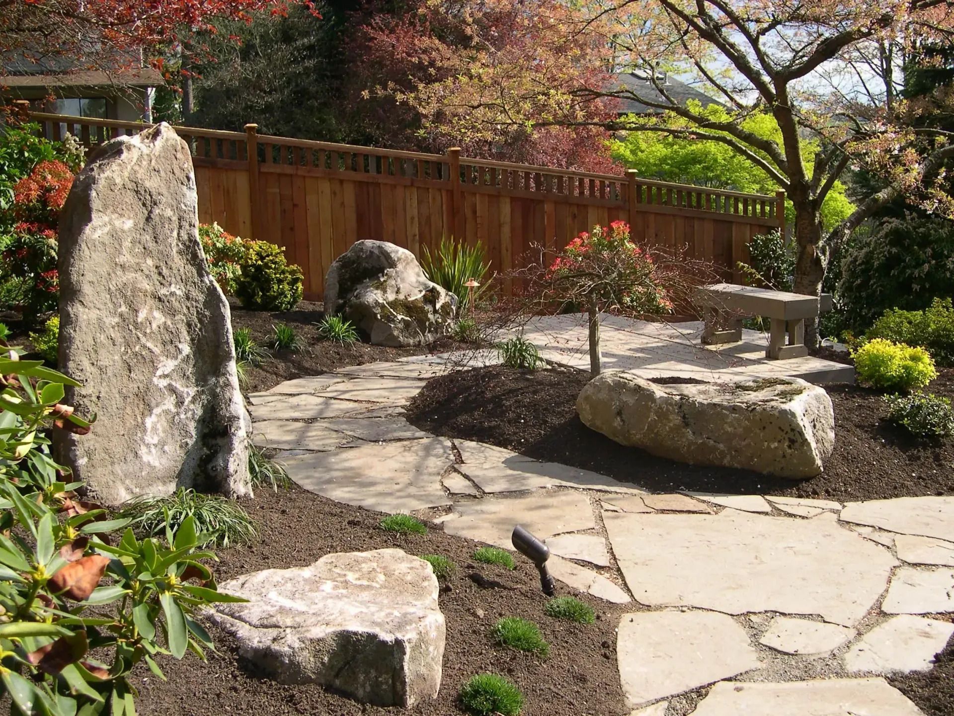Stone garden path with large rocks, a wooden fence, and trees in autumn colors