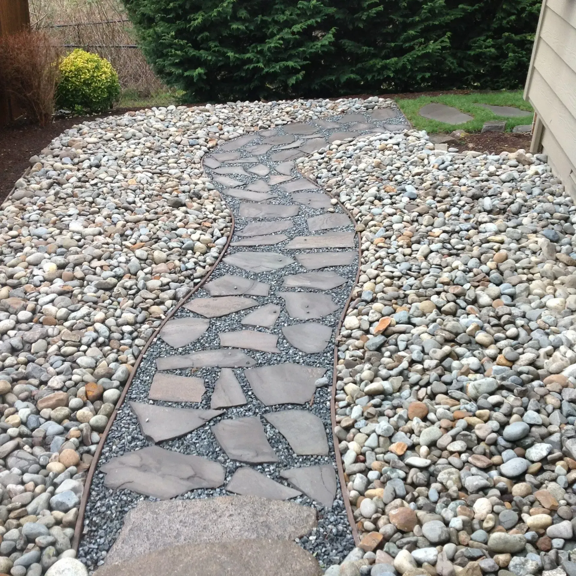 Curved stone walkway through a pebble-covered garden beside a house