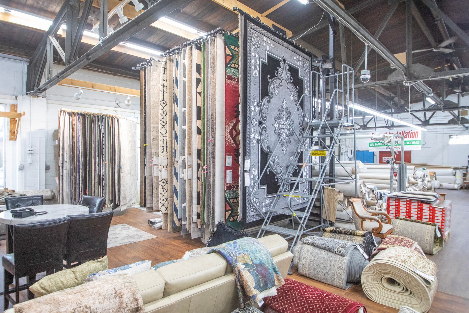 Warehouse interior with rows of rugs displayed for sale, plus a sofa and furniture.