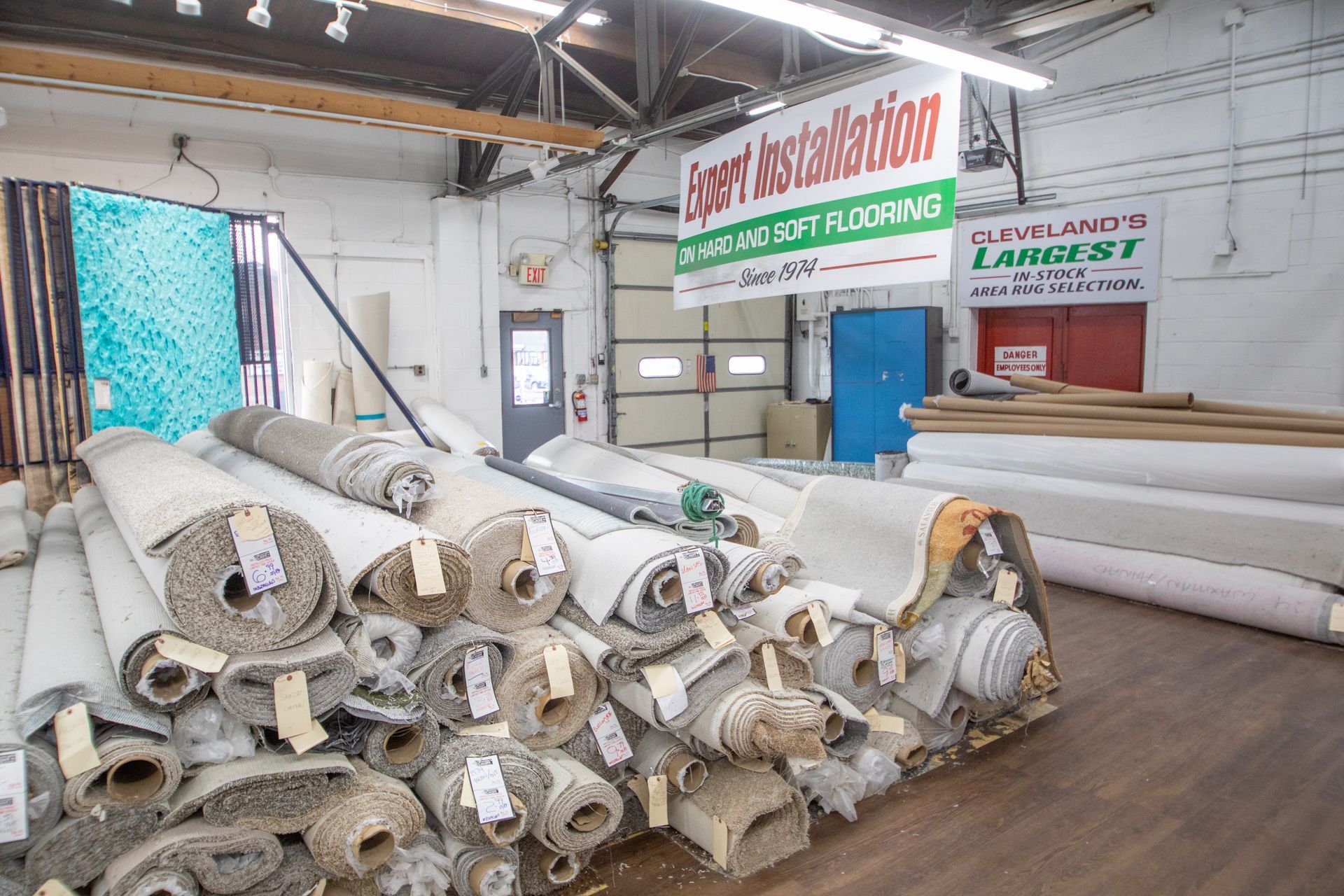 Warehouse interior with rolls of carpet stacked; signs above.