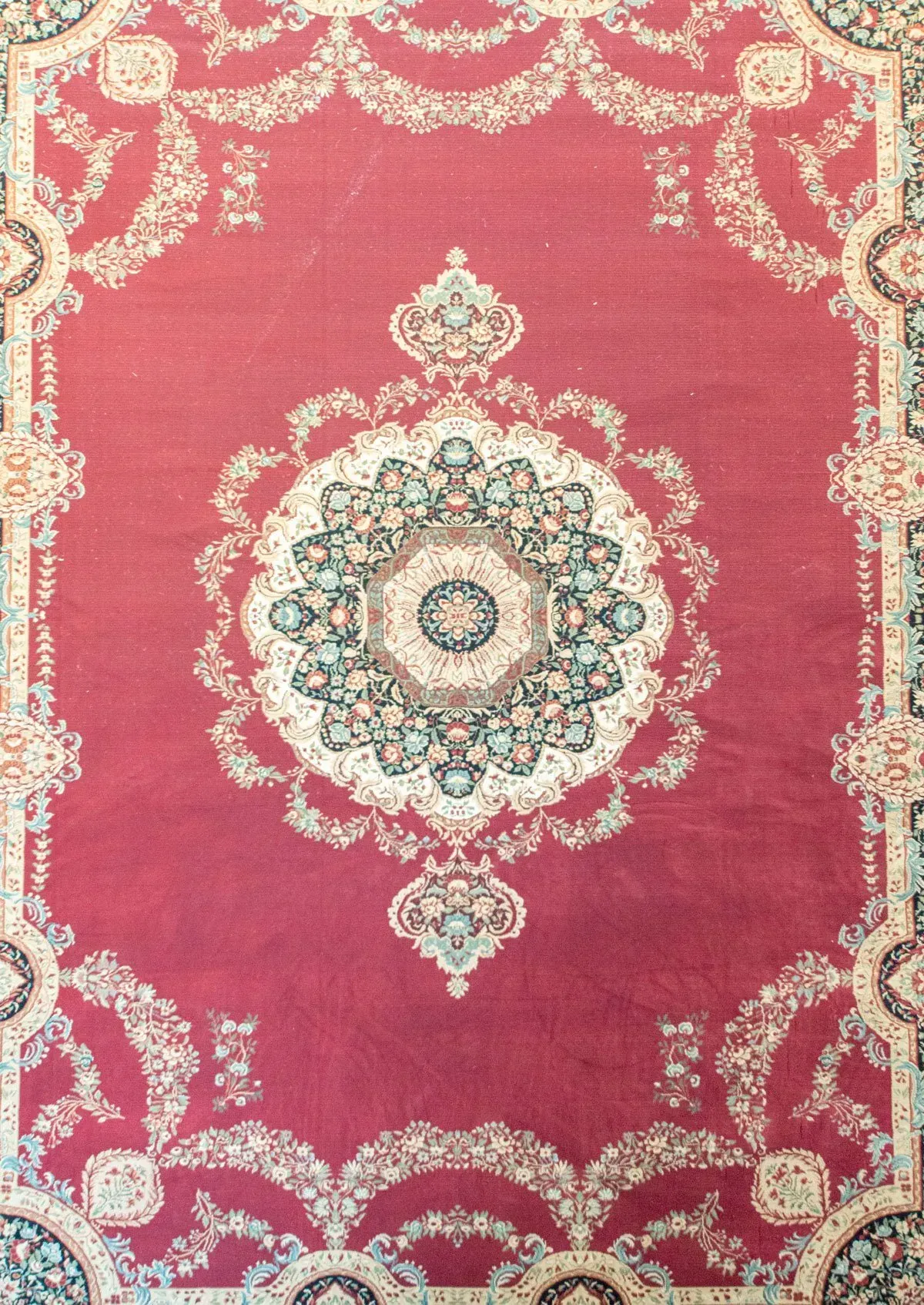 Red rug with central circular medallion and ornate border pattern in beige, teal, and brown.