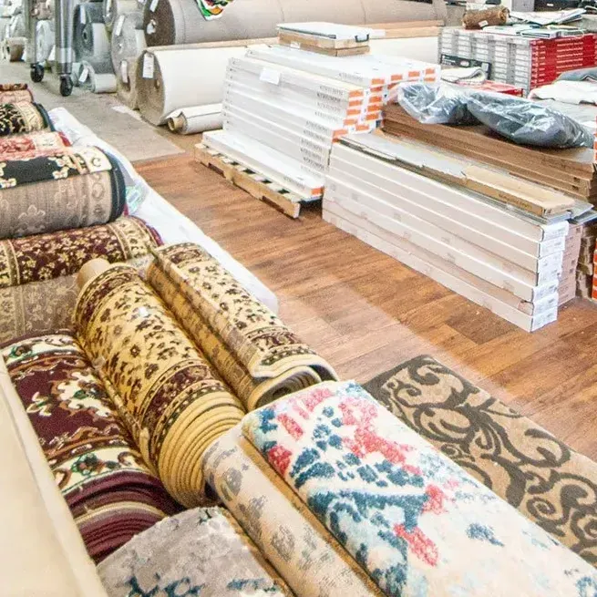 Carpet store interior with rolled rugs, flooring samples, and rolls of carpet.
