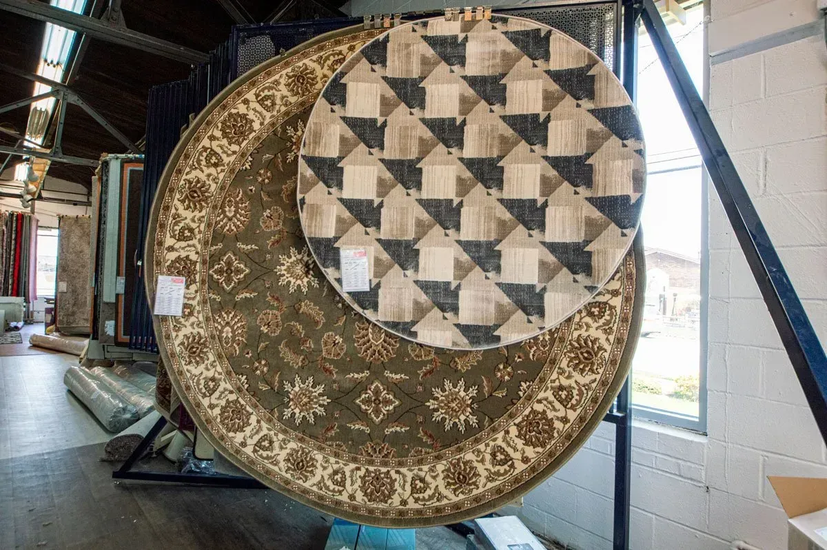 Two round rugs hanging for display; one green patterned, the other with a house-shaped pattern.