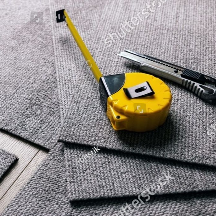 Yellow tape measure and utility knife on gray carpet.