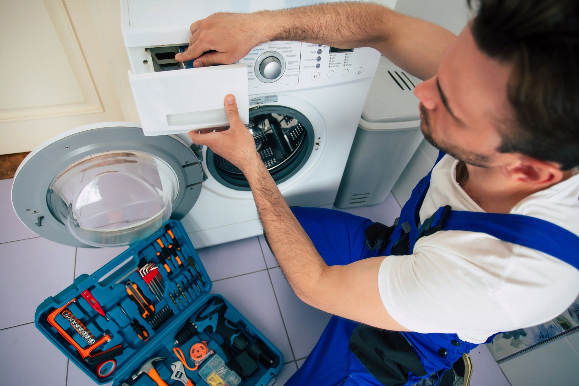 Two Young Male Movers In Uniform Placing Dishwasher In Kitchen