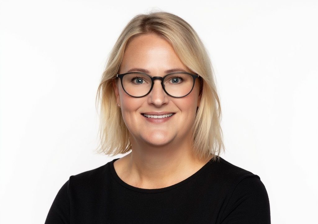 Billede af Anni Jørgensen. Blond kvinde med briller i en sort skjorte smiler, orange baggrund.