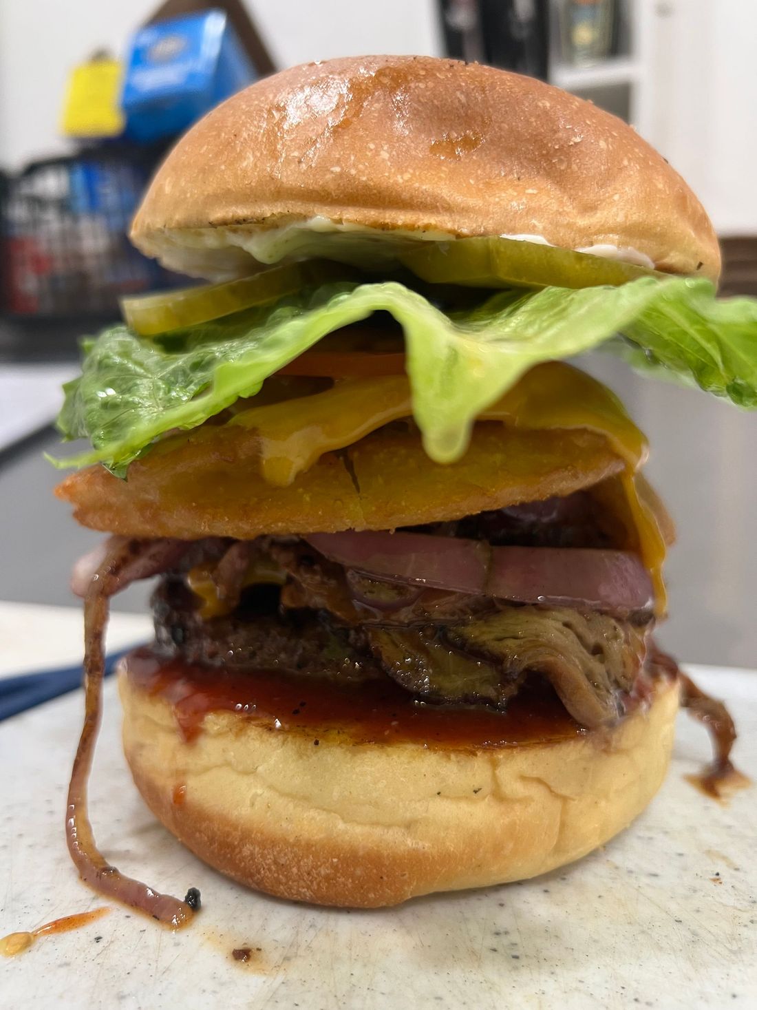 Tall cheeseburger with lettuce, tomato, bacon, and melted cheese on a bun on a kitchen counter