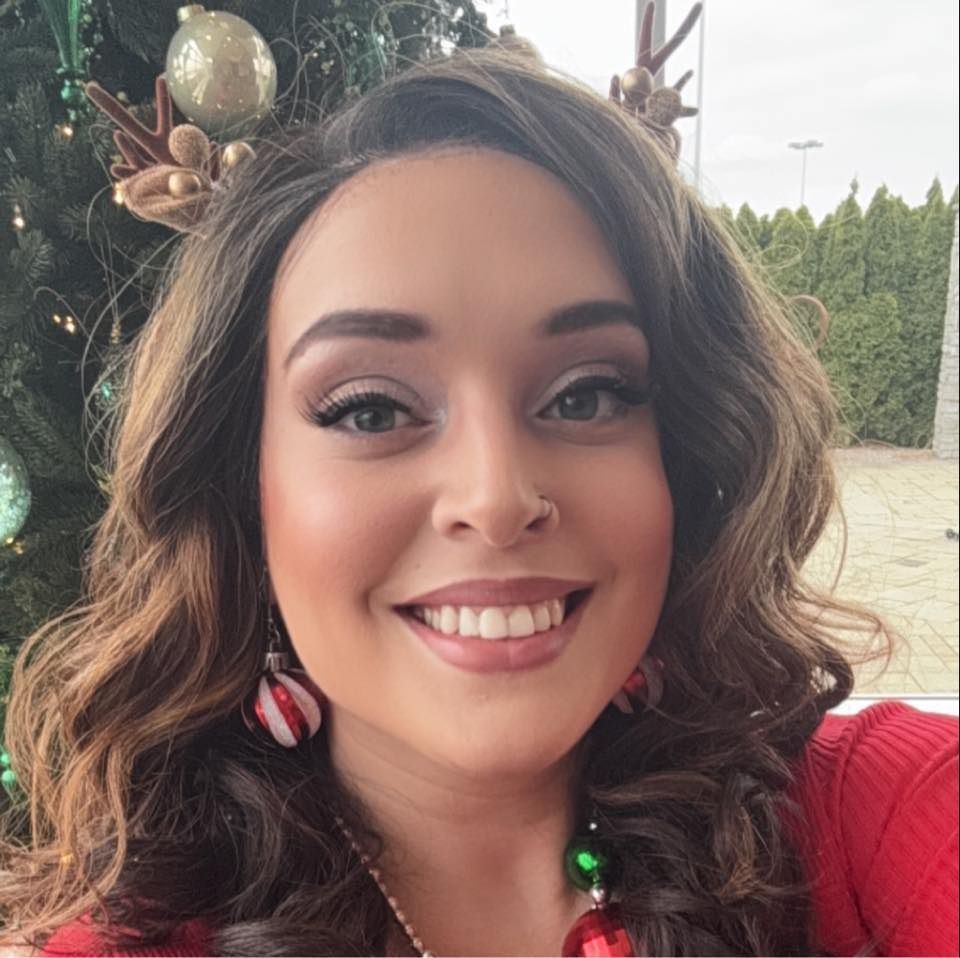 Smiling woman in a red top with festive antler headband, outdoors near greenery