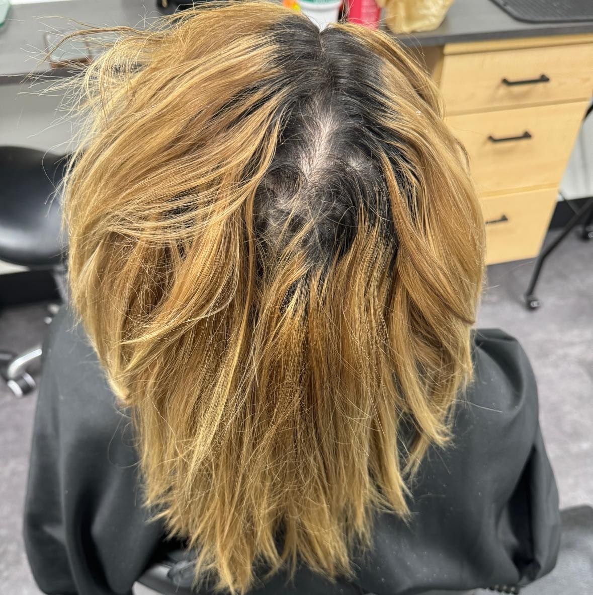 Top view of a person with two-tone blonde and dark hair seated in a salon chair.