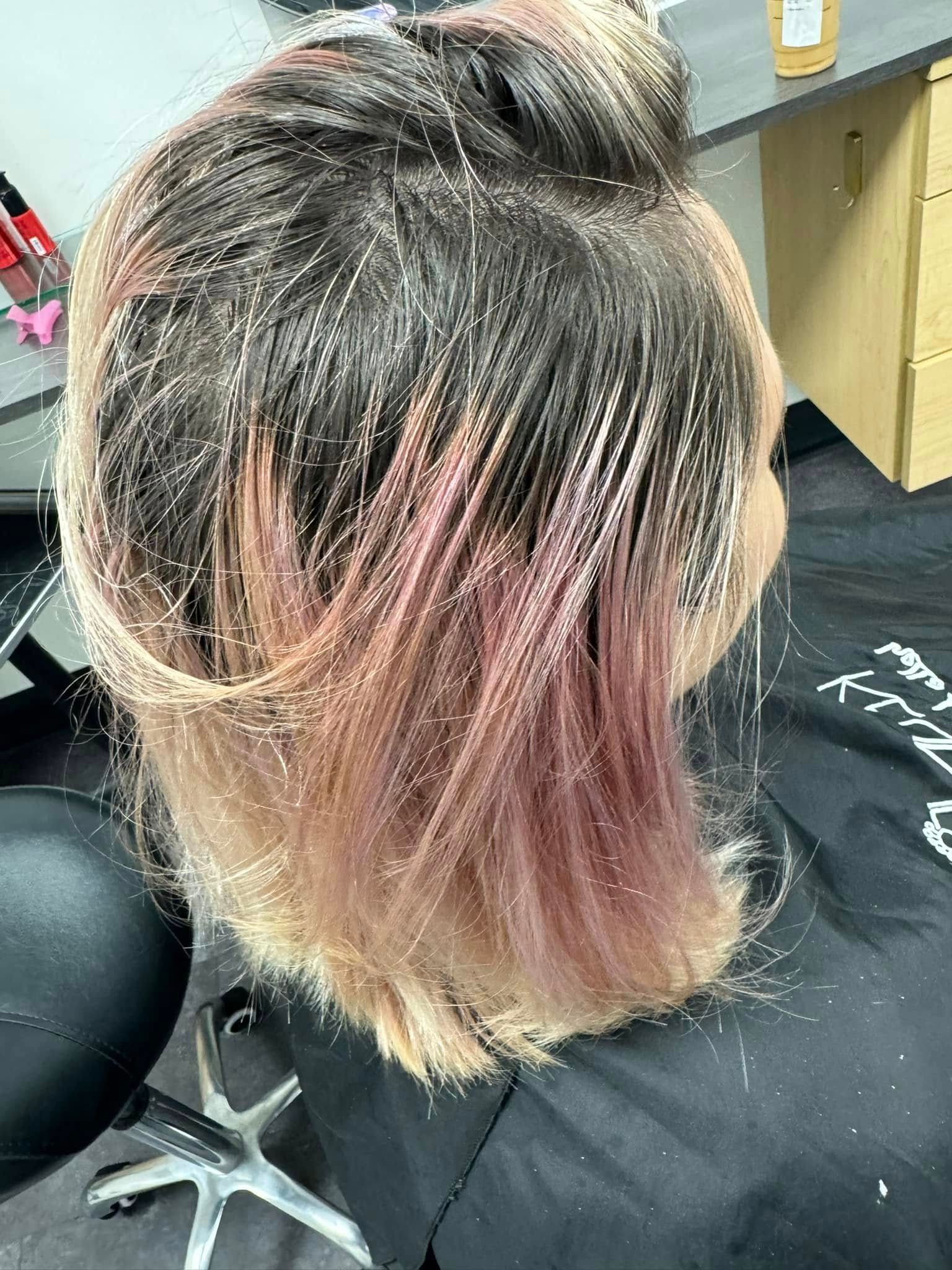 Close-up of a seated person’s dyed hair with dark roots and pink-blonde ends in a salon chair