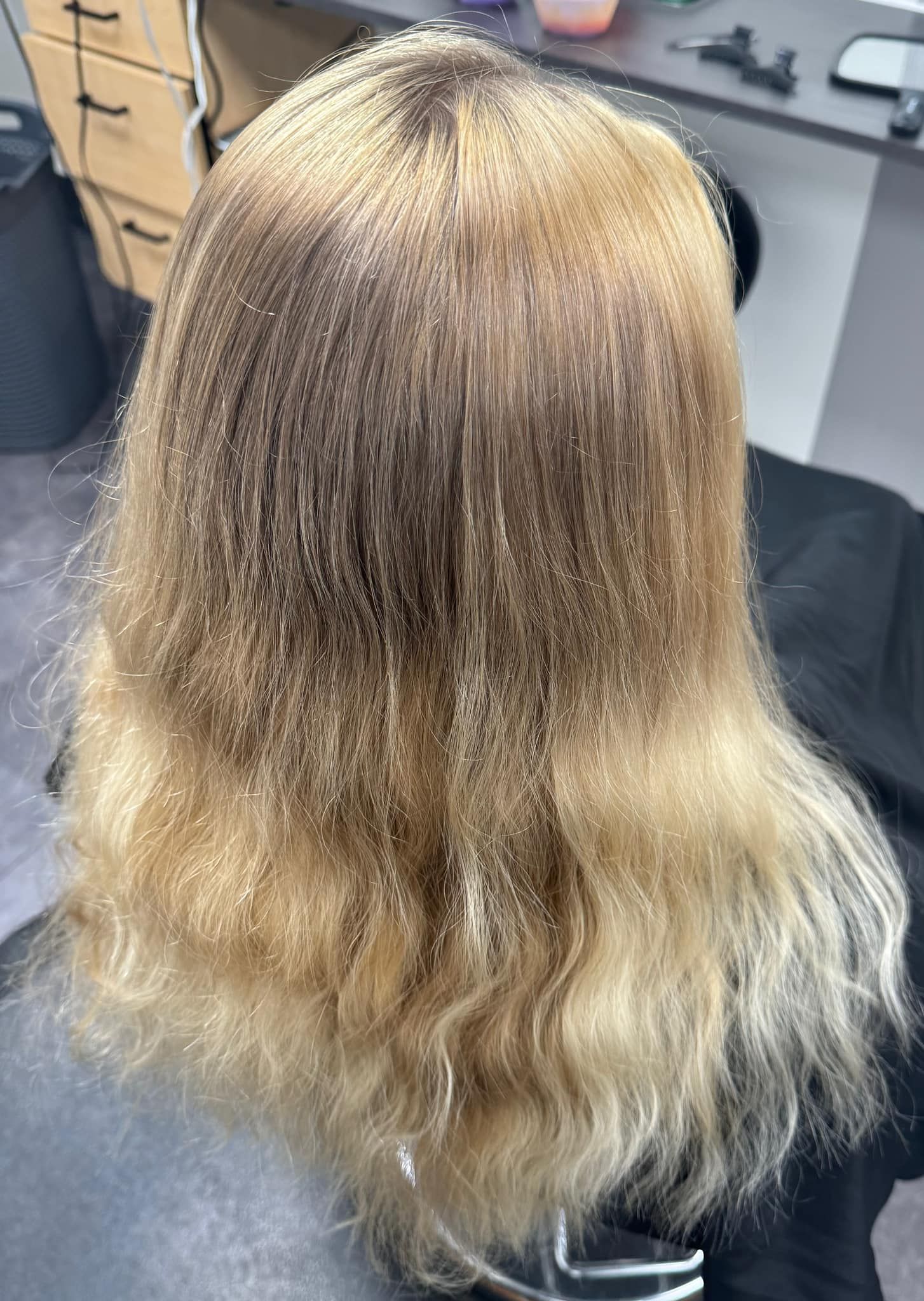 Back view of wavy blonde hair in a salon chair, with darker roots and lighter ends.
