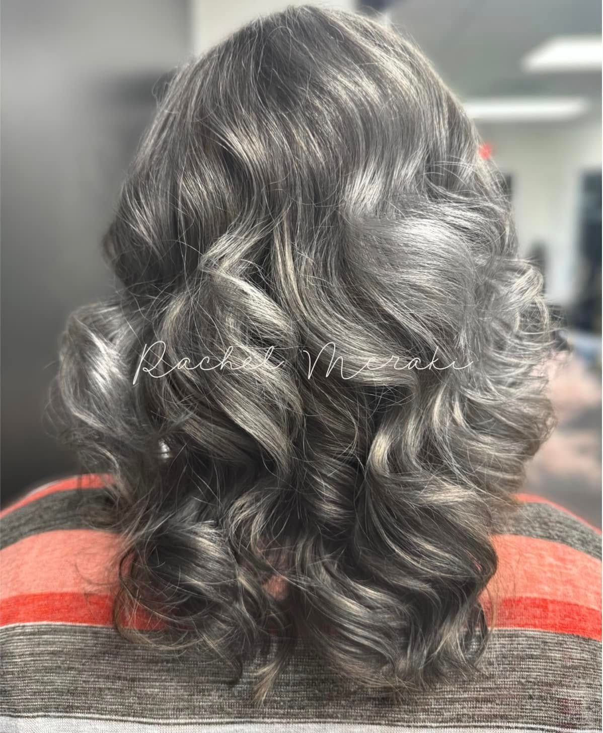 Dark wavy shoulder-length hairstyle with loose curls, viewed from behind, wearing a red and gray striped top