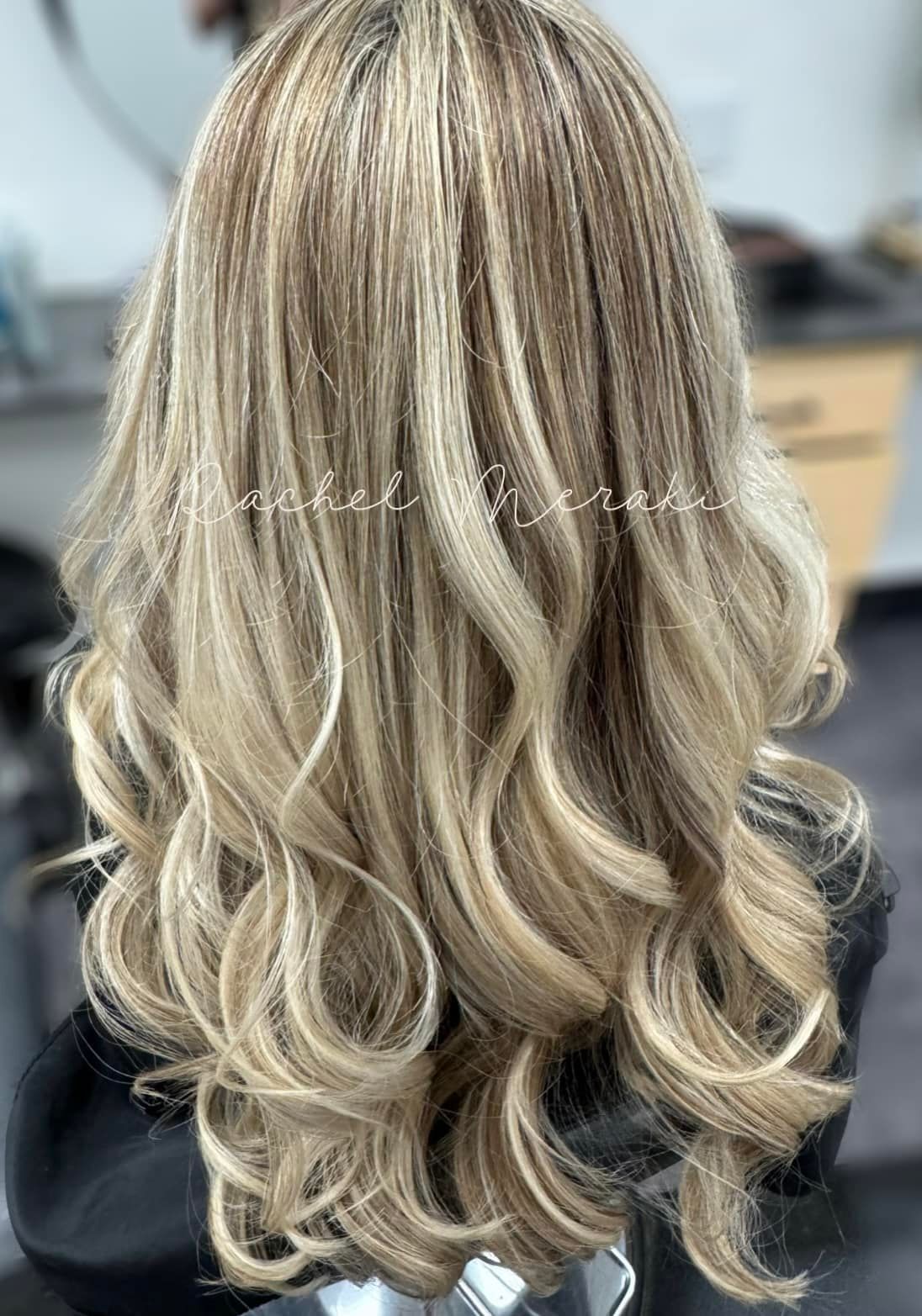 Long wavy blonde hair with dark roots, shown from the back in a salon setting
