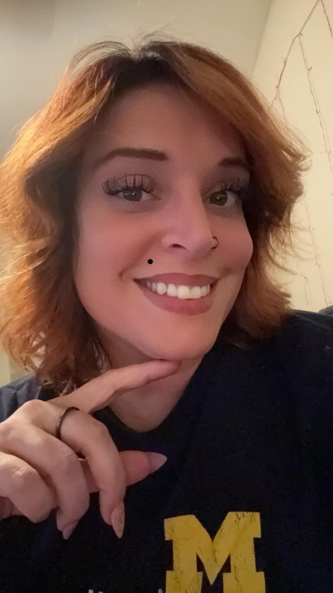 Smiling person with short auburn hair wearing a black shirt with a yellow “M” logo.