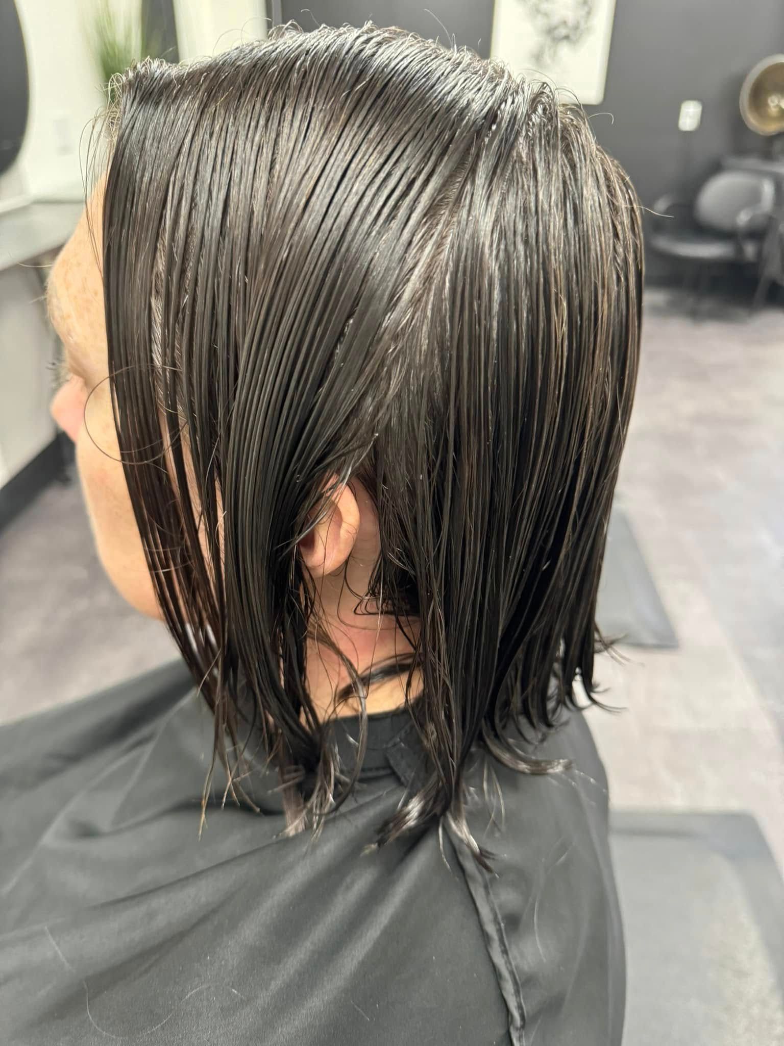 Wet, dark hair being cut in a salon chair, side view with a black cape.