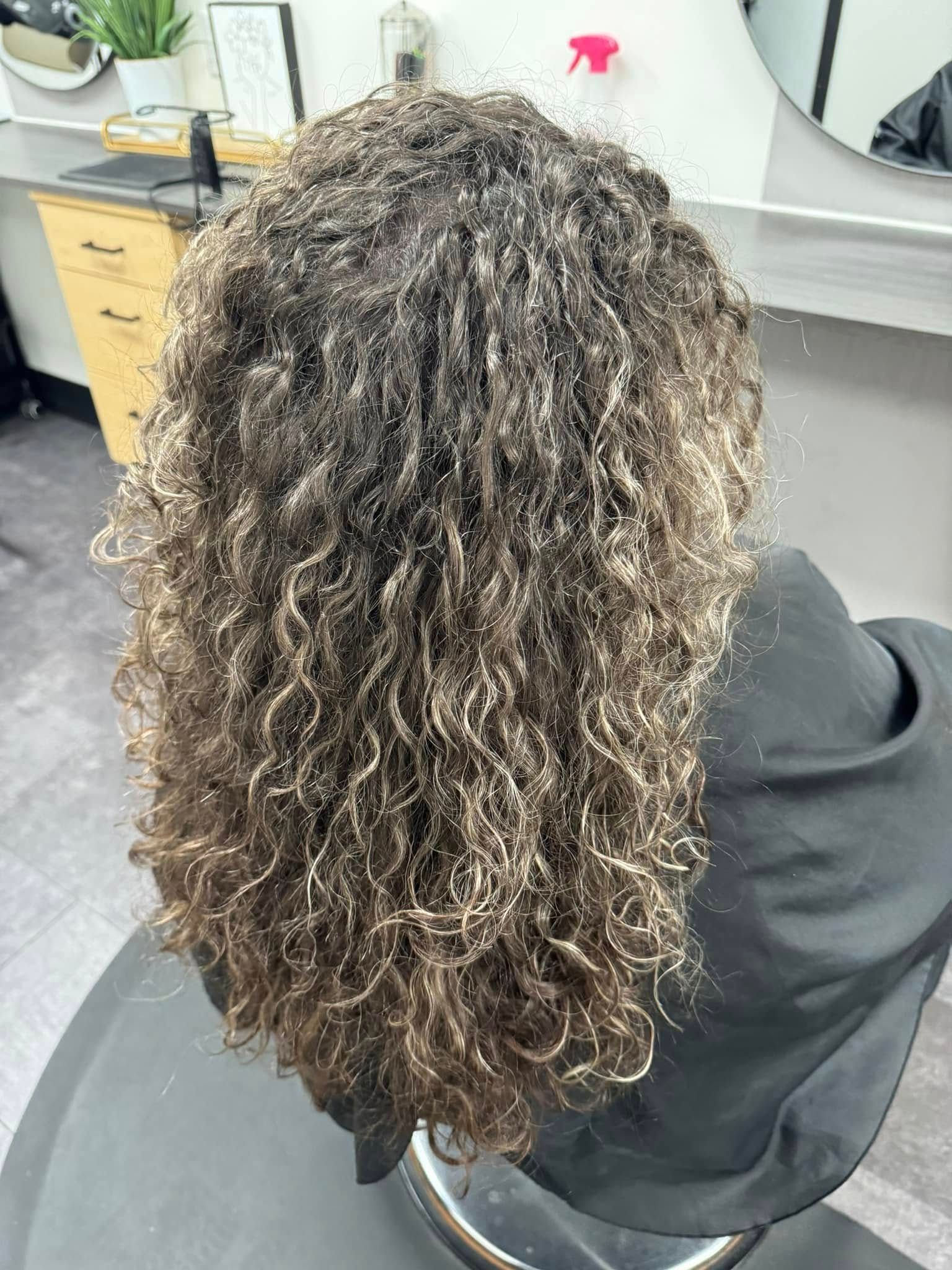 Curly brown hair from behind, seated in a salon chair with wet or damp curls.