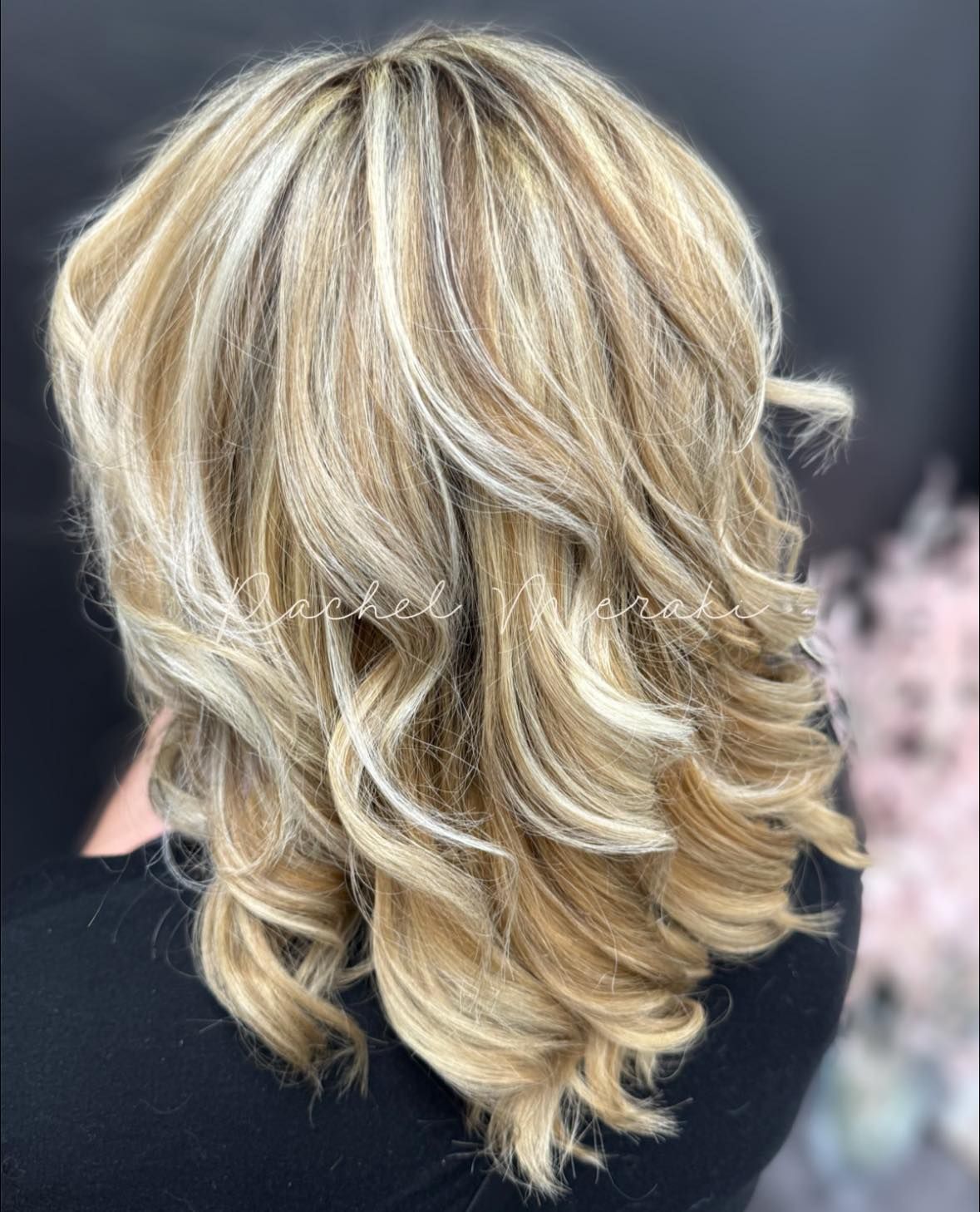Blonde layered hairstyle with soft curls and highlights against a dark background