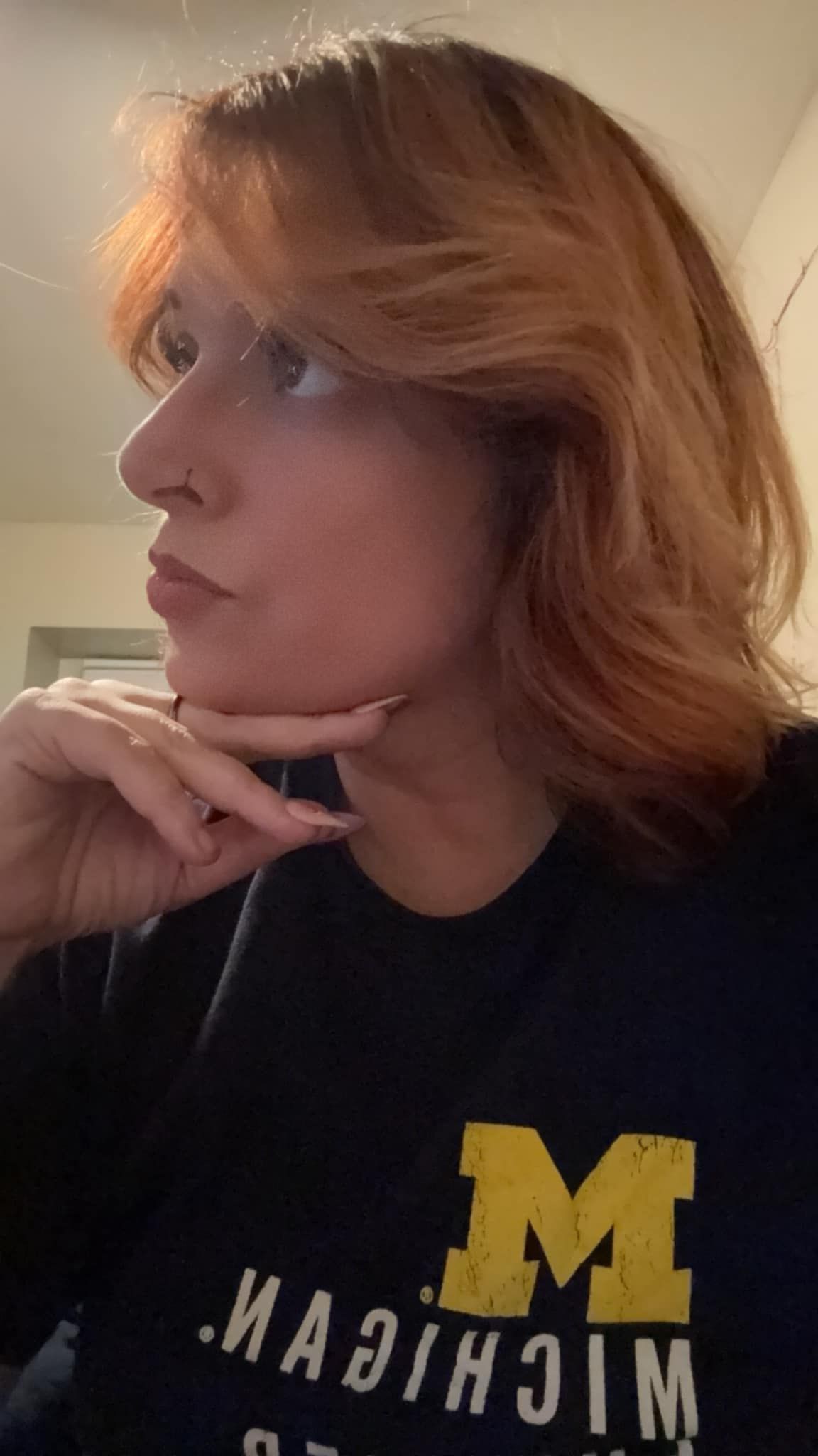 Person in profile, resting chin on hand, wearing a black Michigan sweatshirt with a yellow “M” logo.