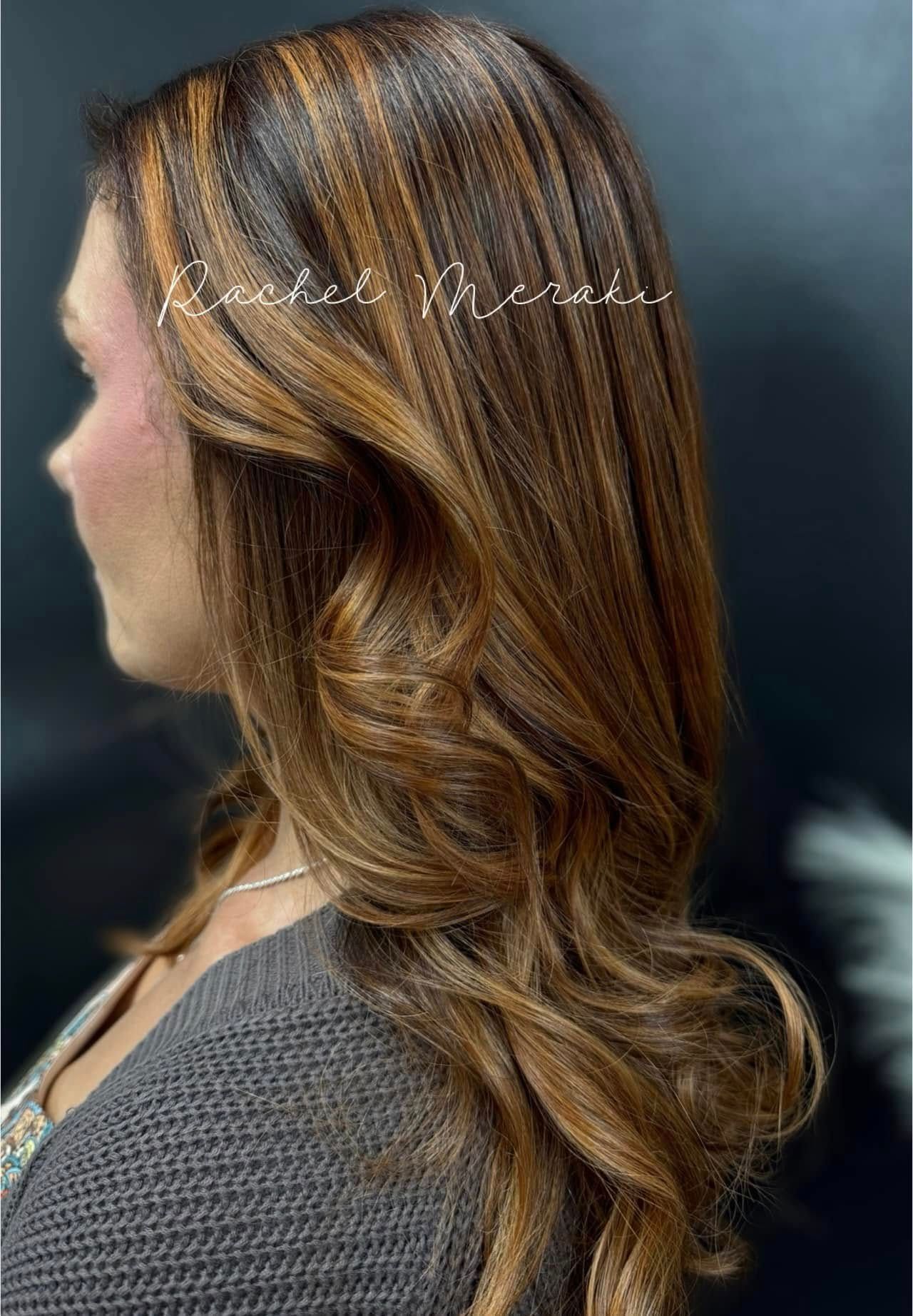 Profile view of a woman with long, wavy brown hair and blonde highlights against a dark background