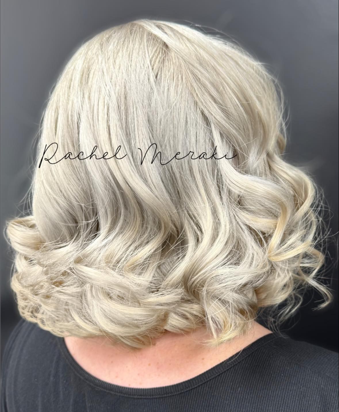 Short layered silver-blonde bob with soft curls at the nape, shown from the back.