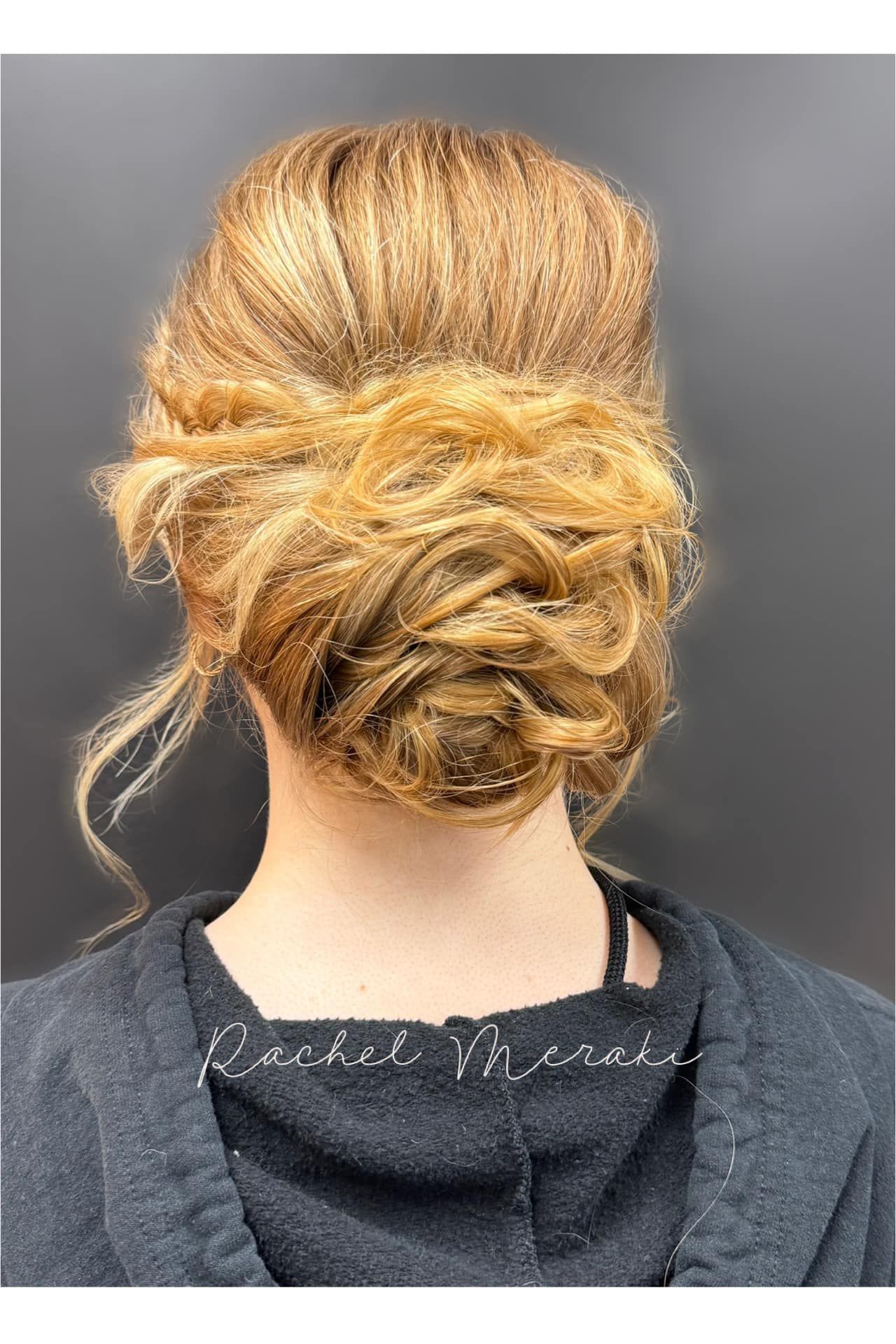 Blonde updo hairstyle with loose curls, shown from the back against a gray background