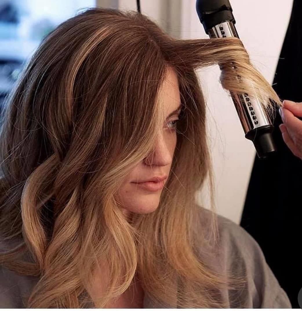Woman with wavy ombré hair being curled with a styling iron in a salon