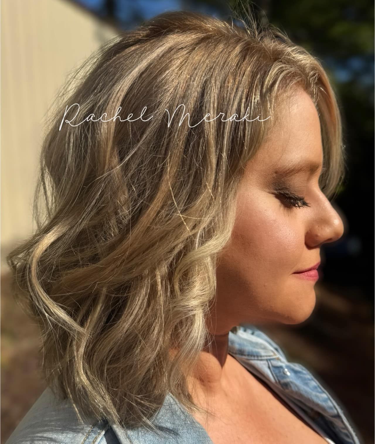 Profile view of a woman with wavy blonde hair in sunlight against a blurred outdoor background