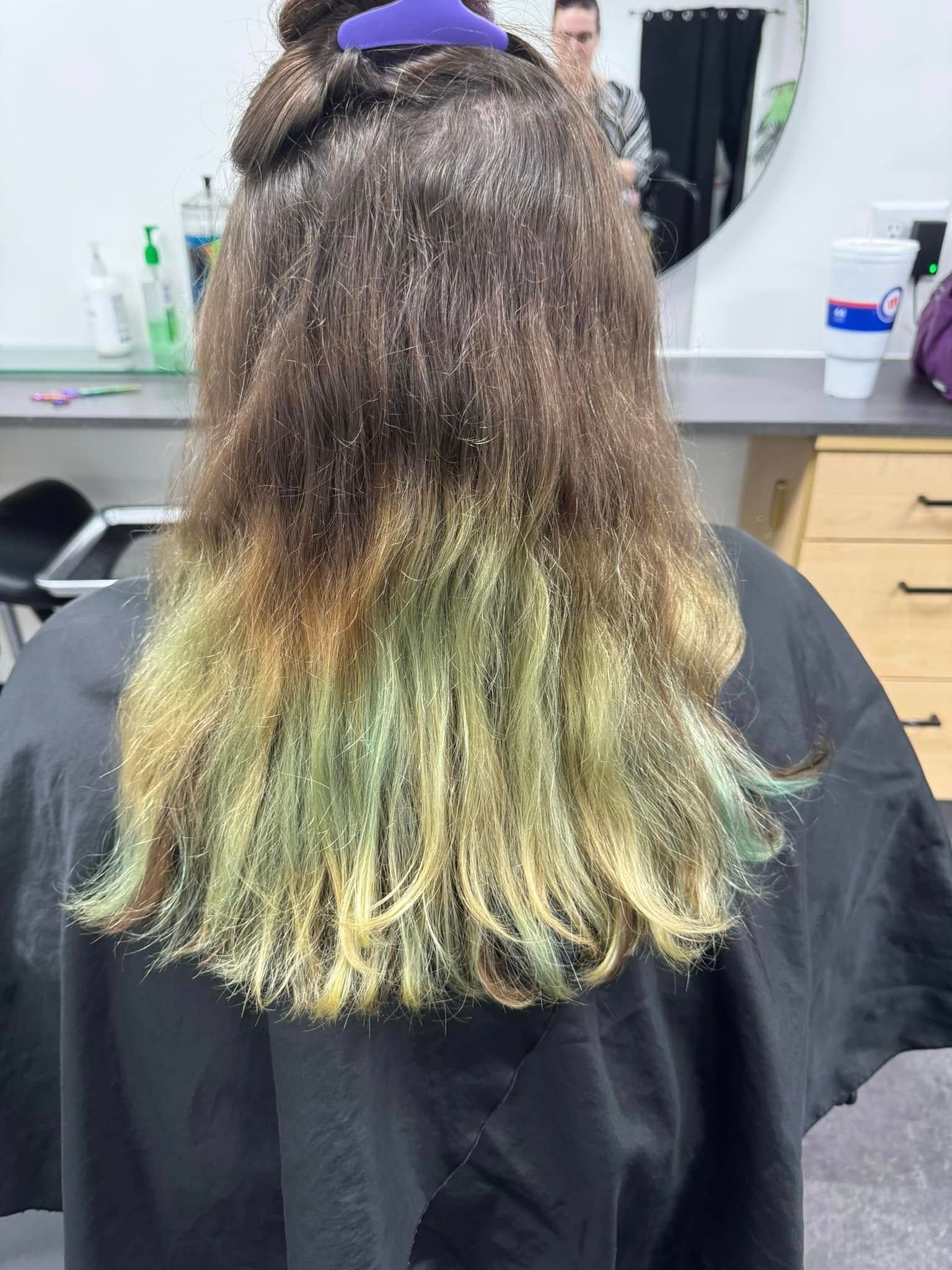 Hairdresser shows long brown hair with green-dyed ends in a salon chair