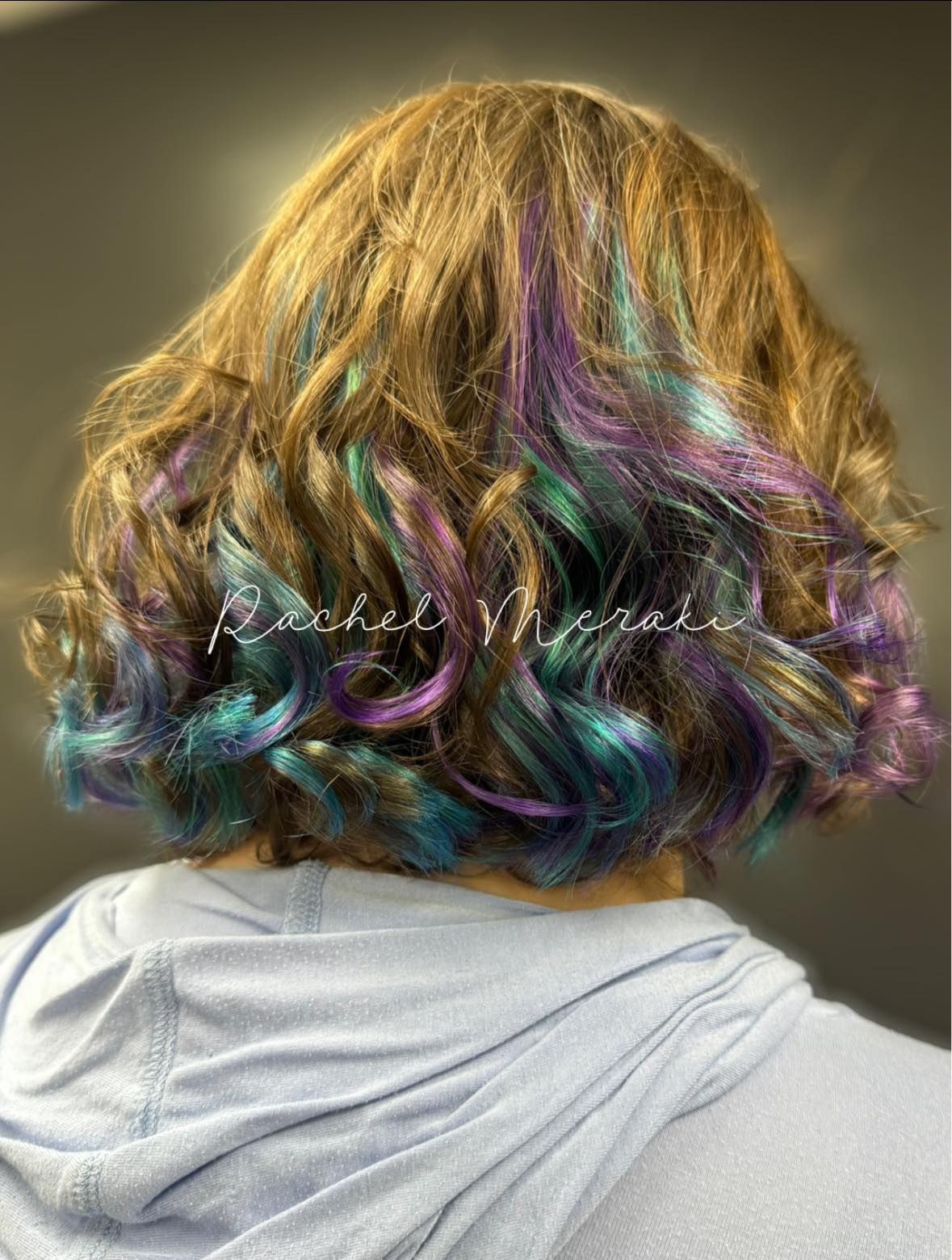Back view of shoulder-length wavy hair with gold, purple, and teal highlights over a gray hoodie
