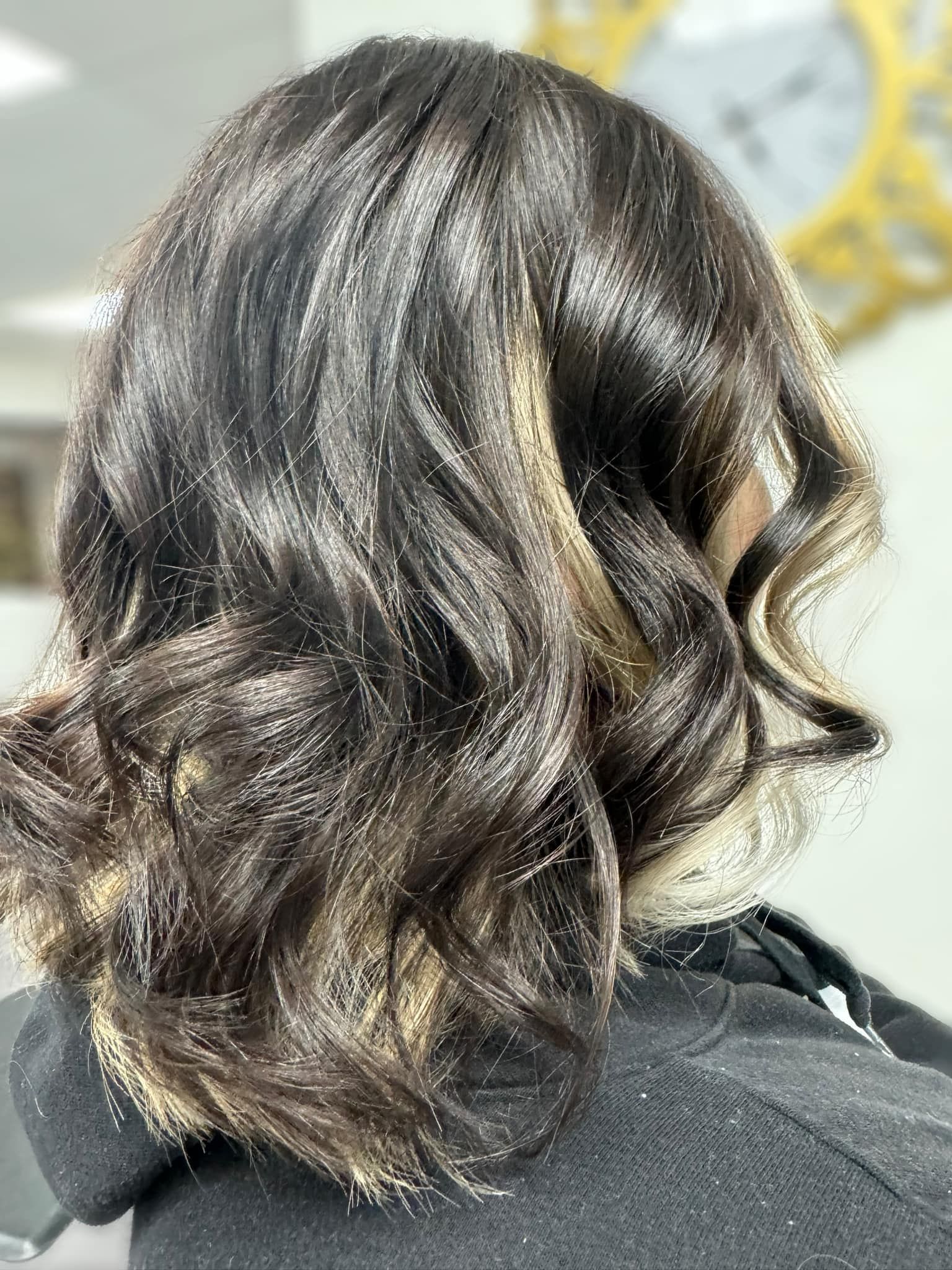 Dark wavy shoulder-length hair with subtle blonde highlights, seen from behind on a black jacket