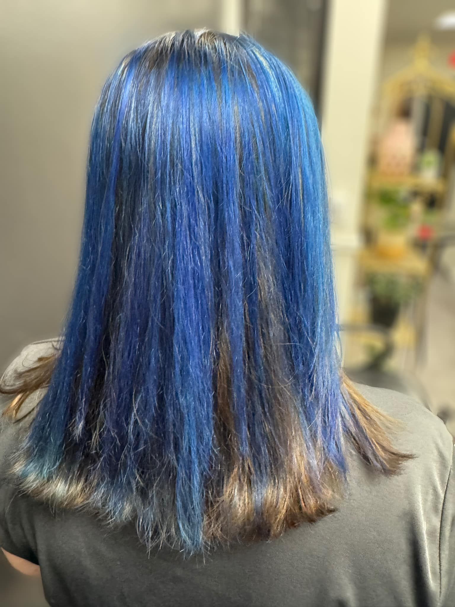 Person with shoulder-length blue hair shown from behind in an indoor setting