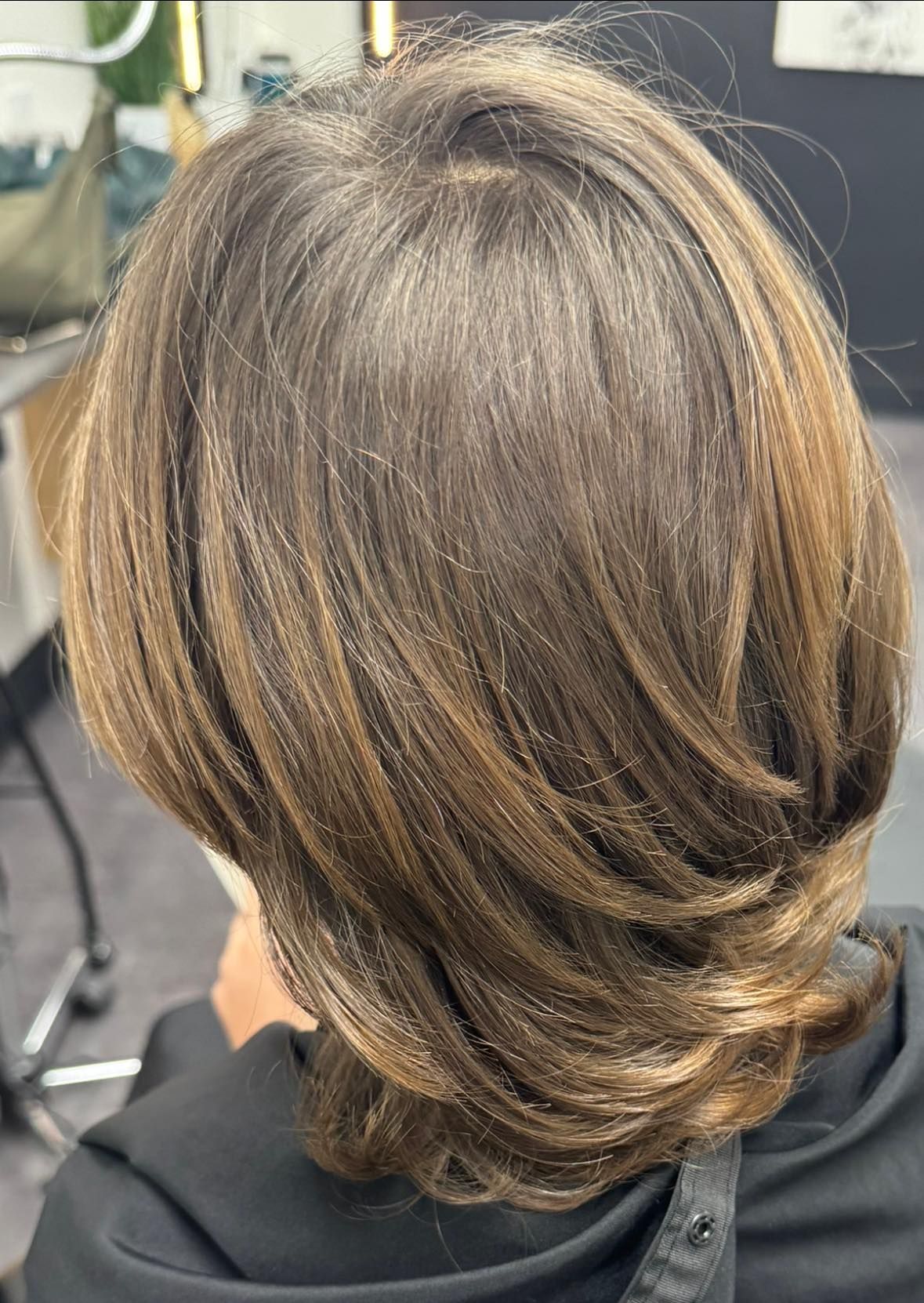 Short layered brown hairstyle with blonde highlights, viewed from the back in a salon chair
