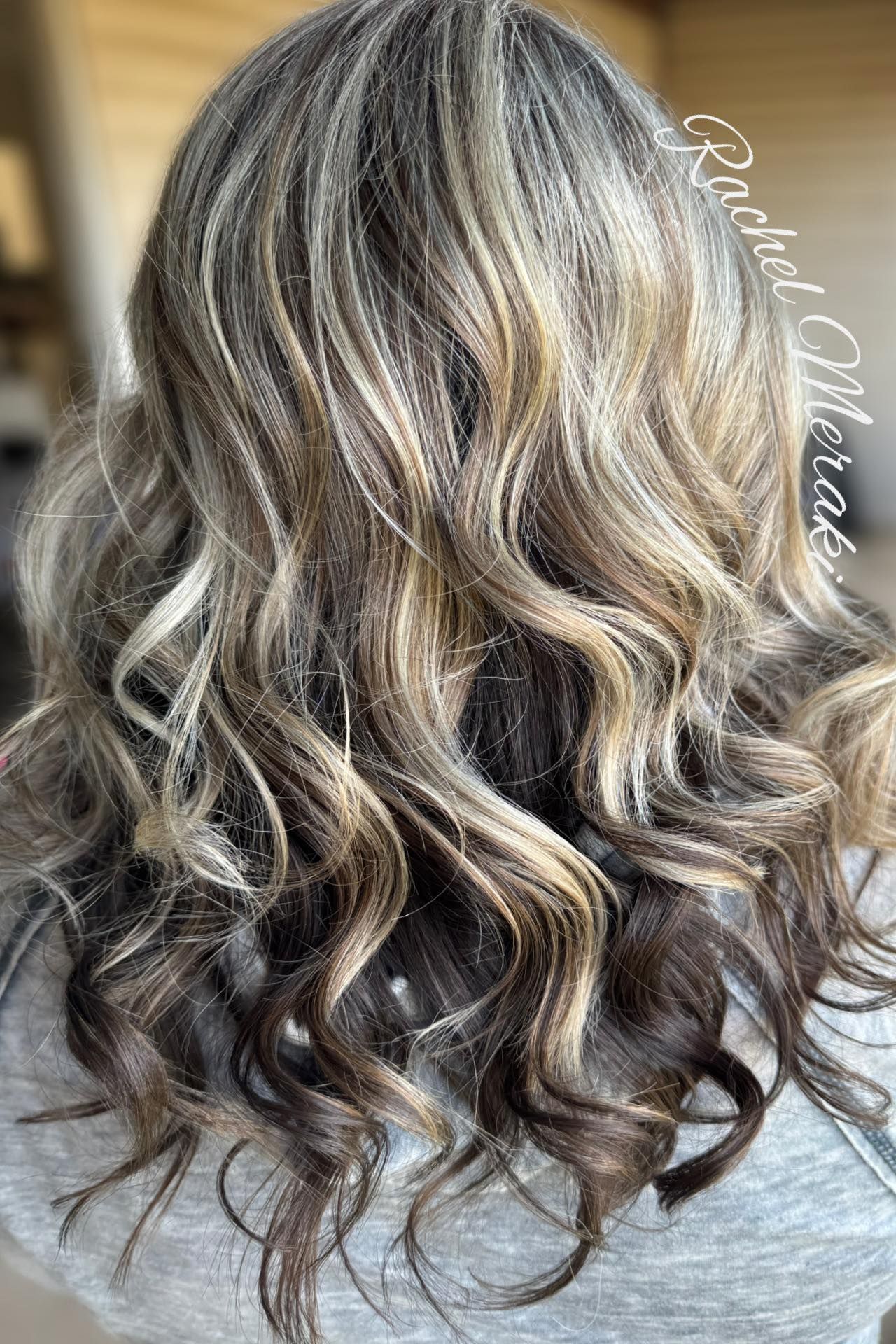 Long wavy blonde and brown highlighted hair with loose curls against a neutral background
