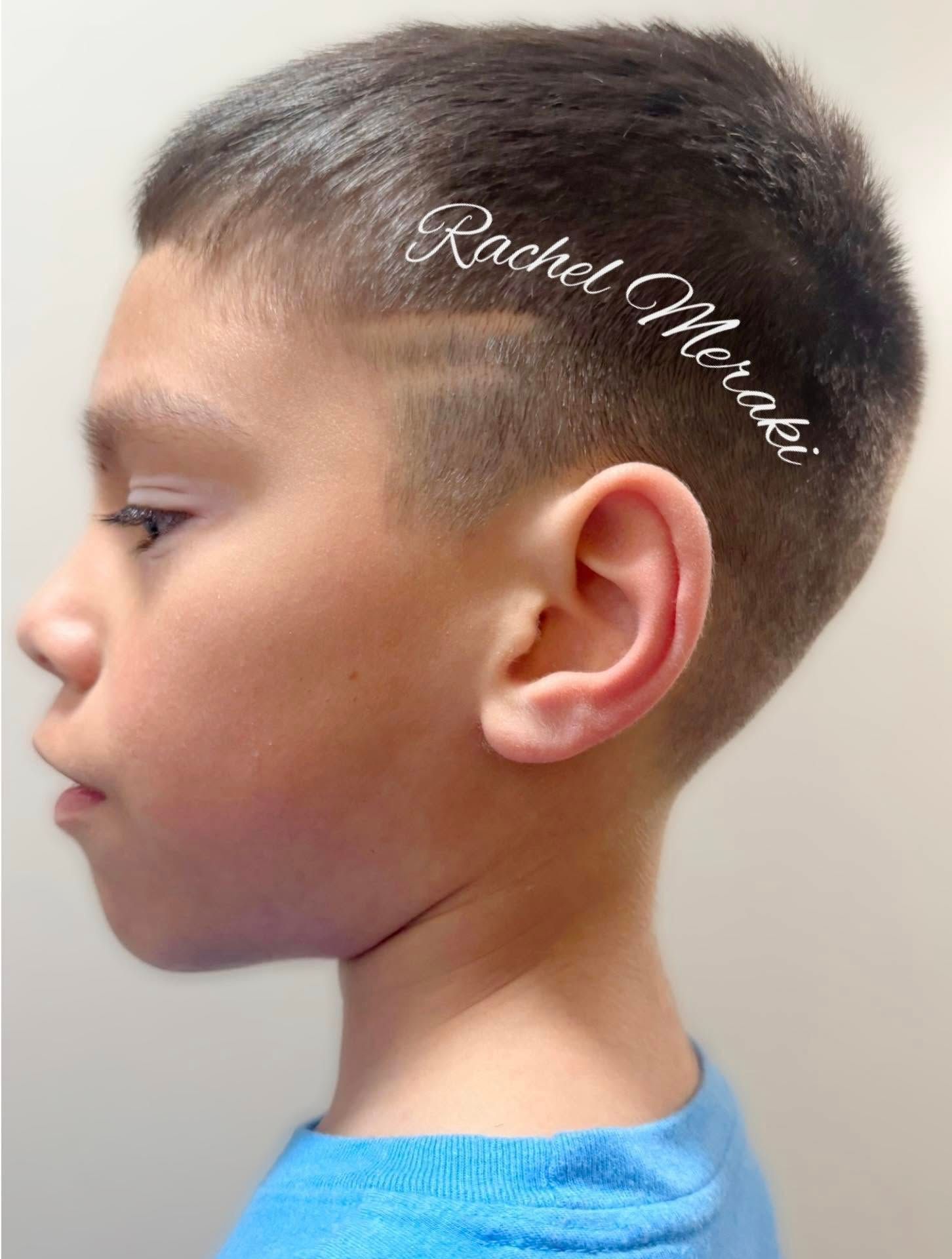 Side profile of a young child with a short haircut and blue shirt against a plain background.