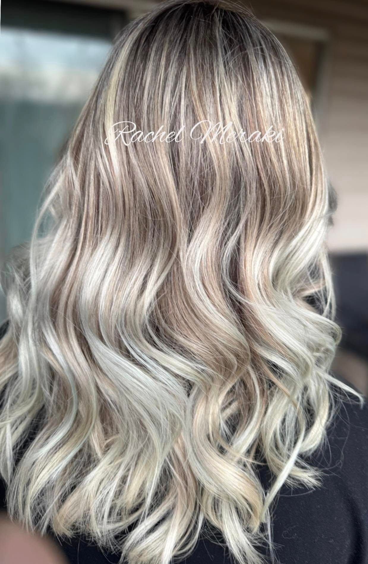 Wavy blonde balayage hairstyle with dark roots, shown from the back.