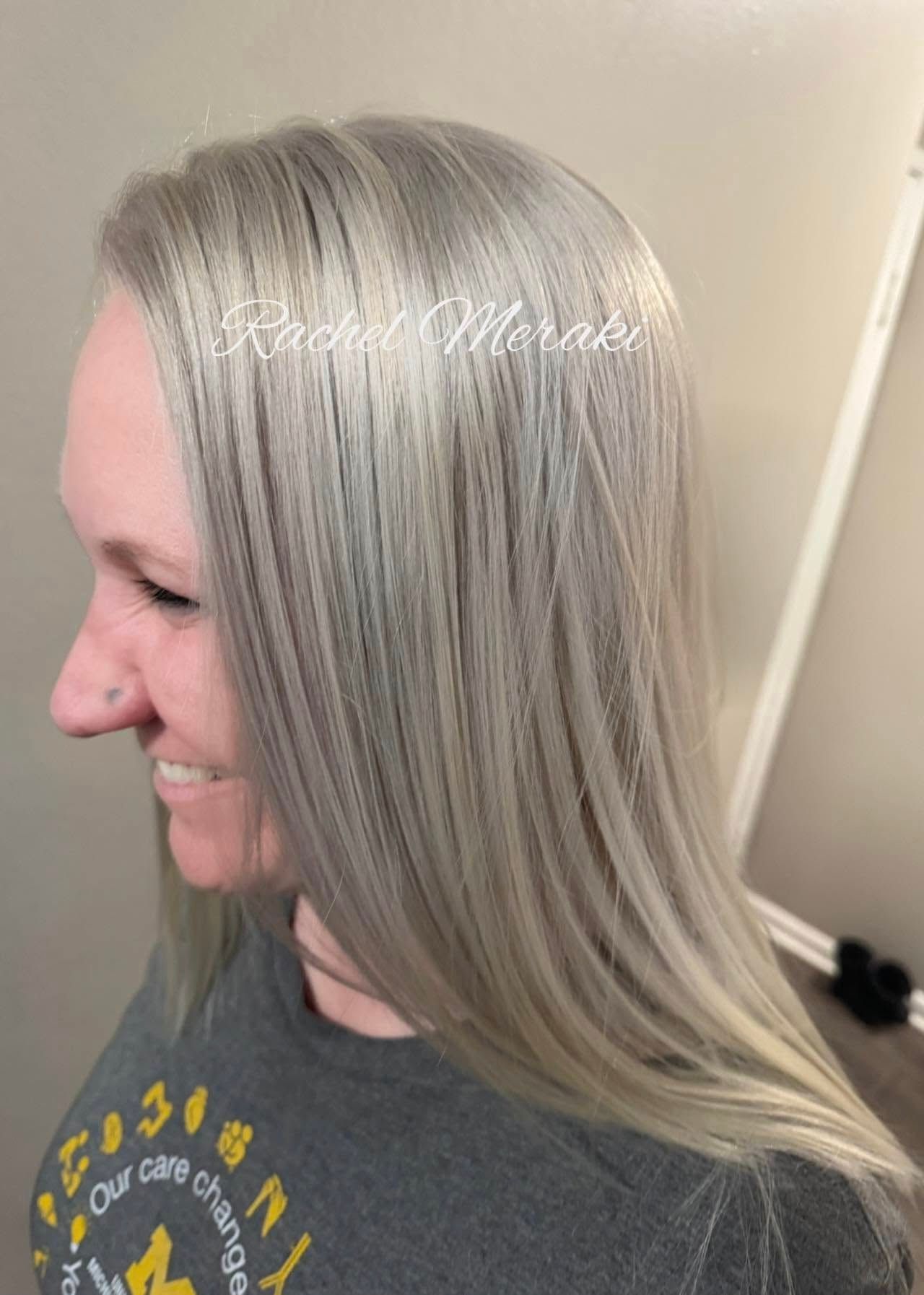 Profile view of a woman with long silver-blonde hair smiling in a salon-like setting