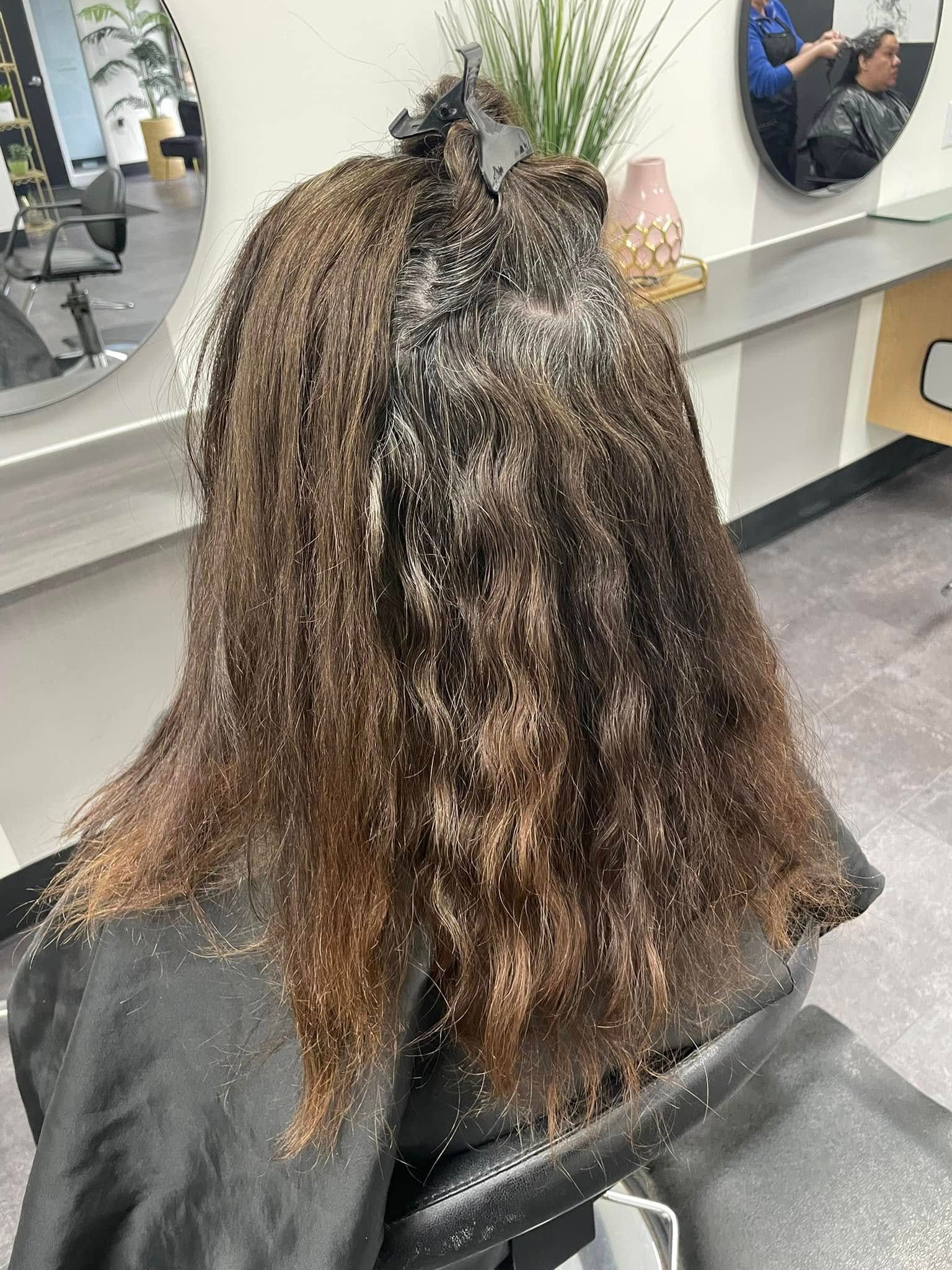 Hair stylist foils a client’s long brown hair in a salon chair.