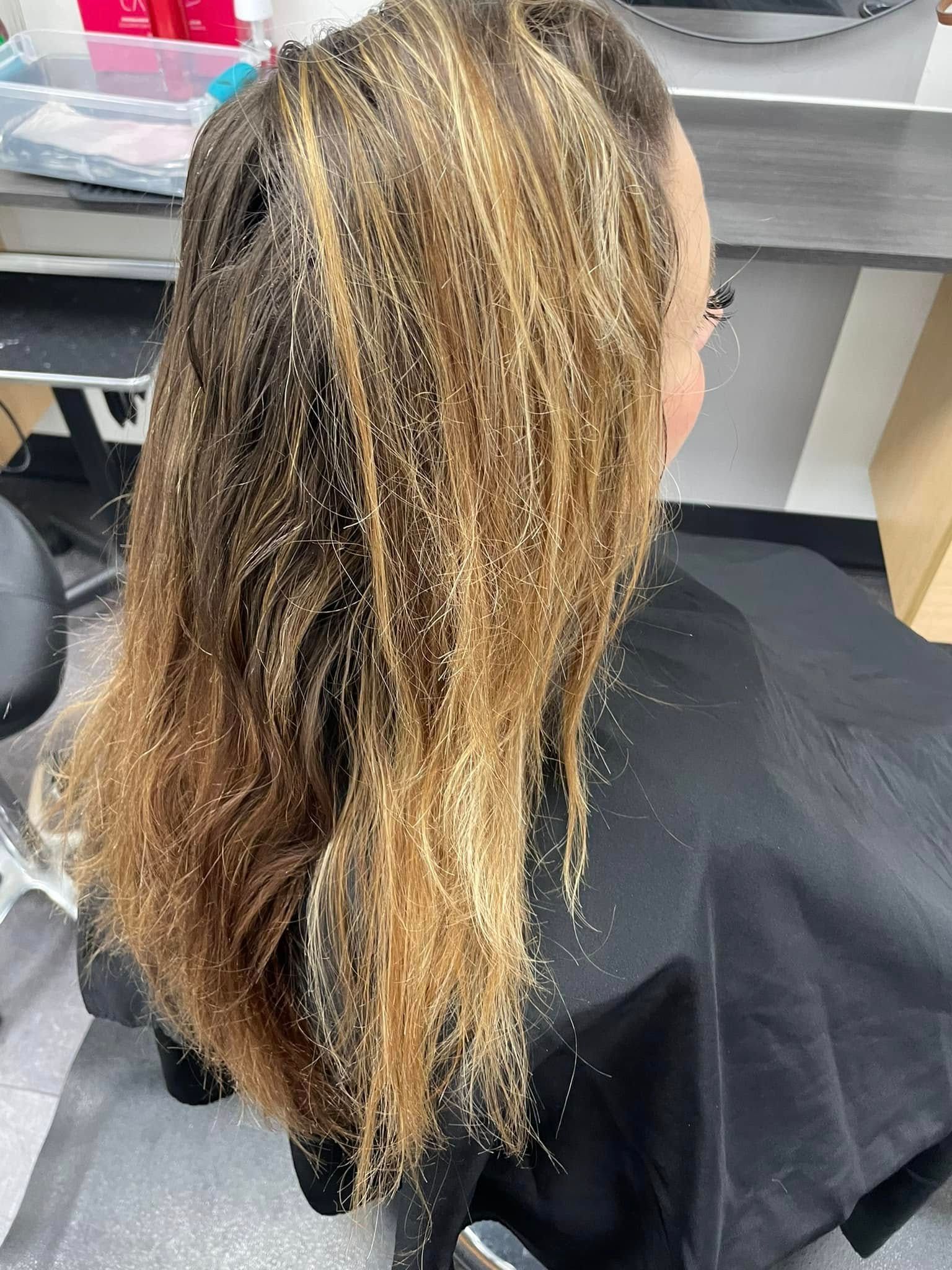 Salon chair with long highlighted hair being worked on, viewed from behind