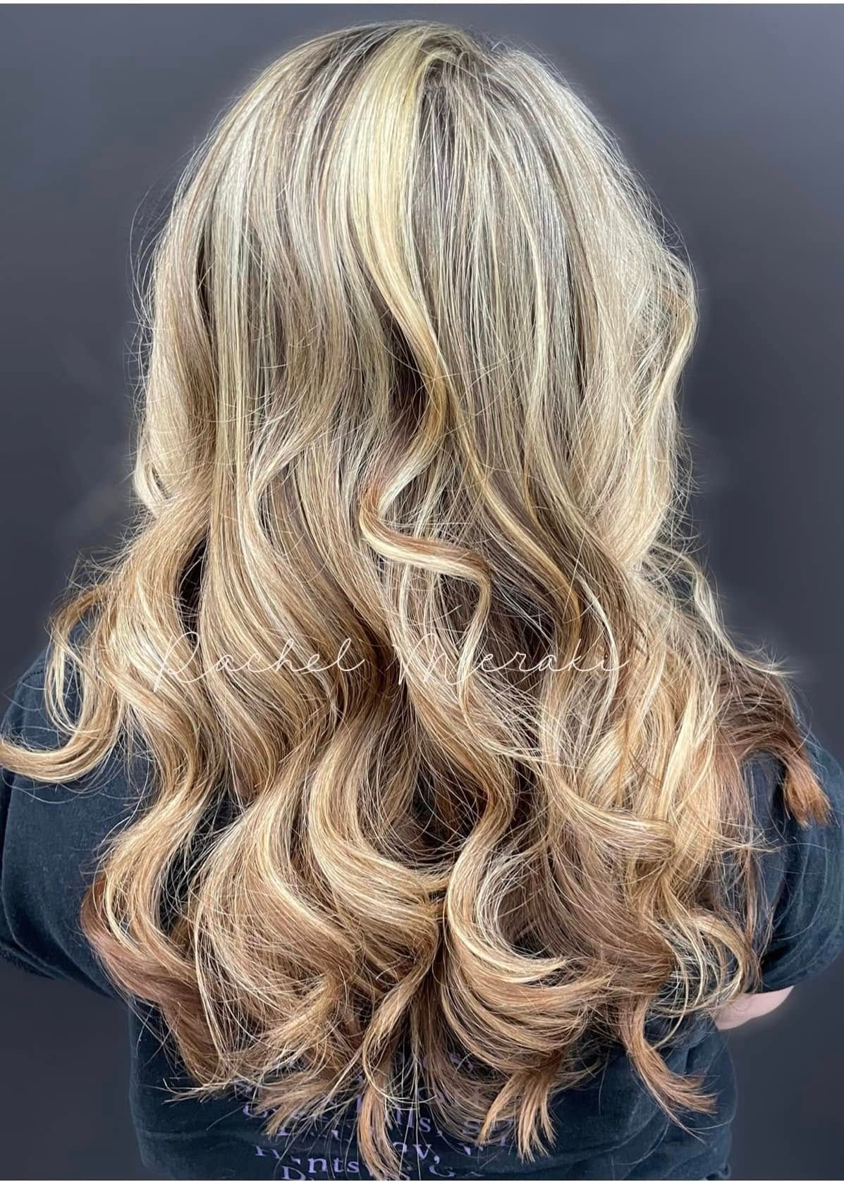 Long wavy blonde hair with darker lowlights, shown from the back against a dark background