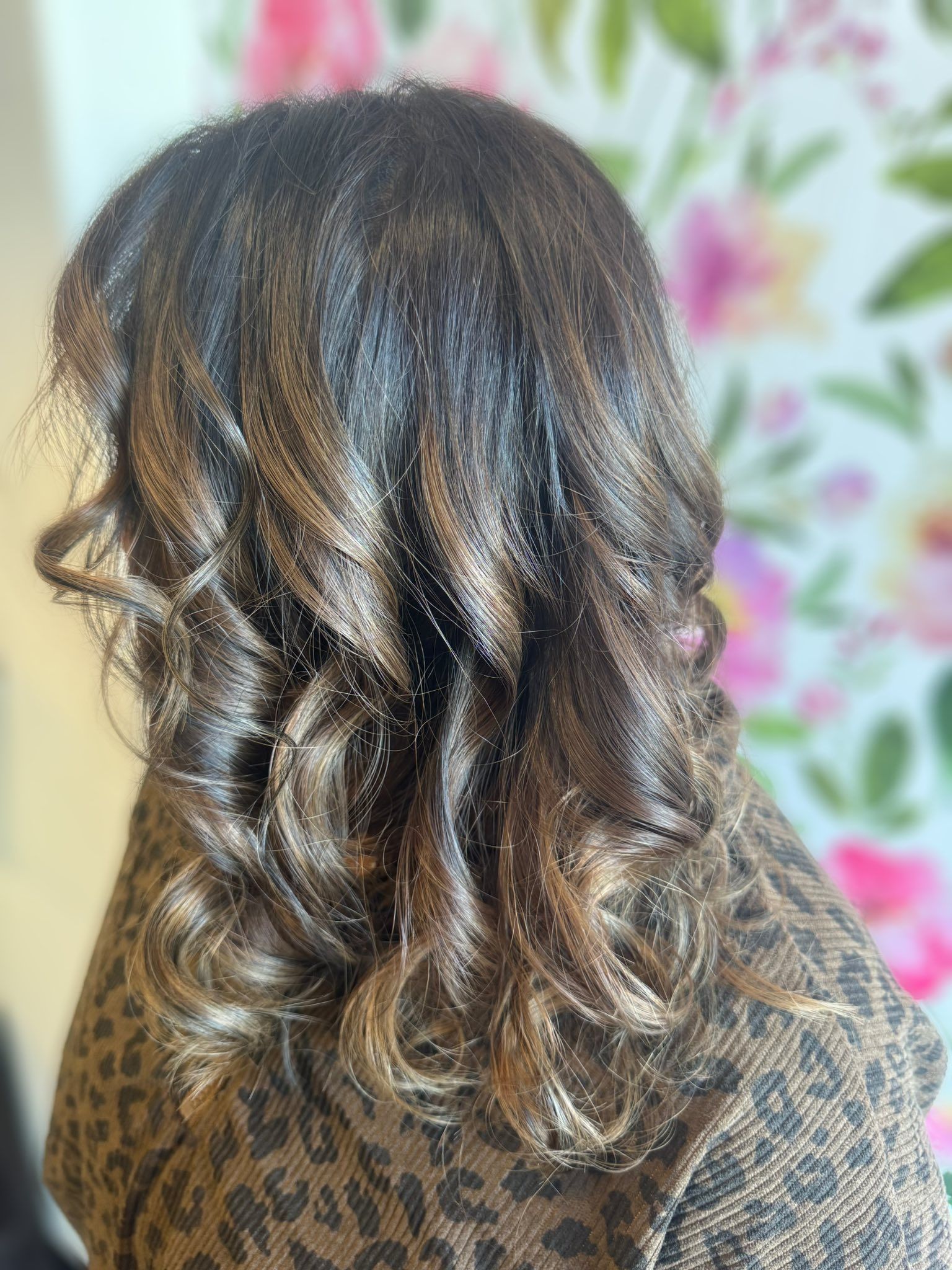 Back view of shoulder-length wavy dark hair with blonde highlights against a floral background